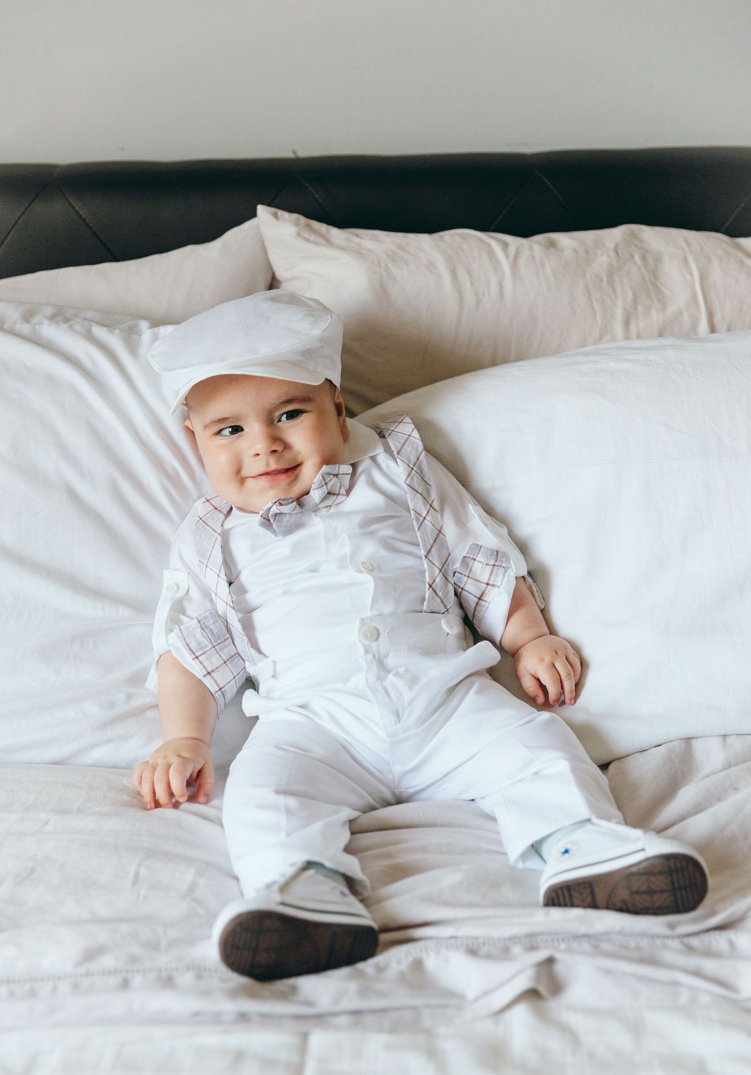 Baby wearing white christening gown lying on white bedding in a series of sweet poses.
