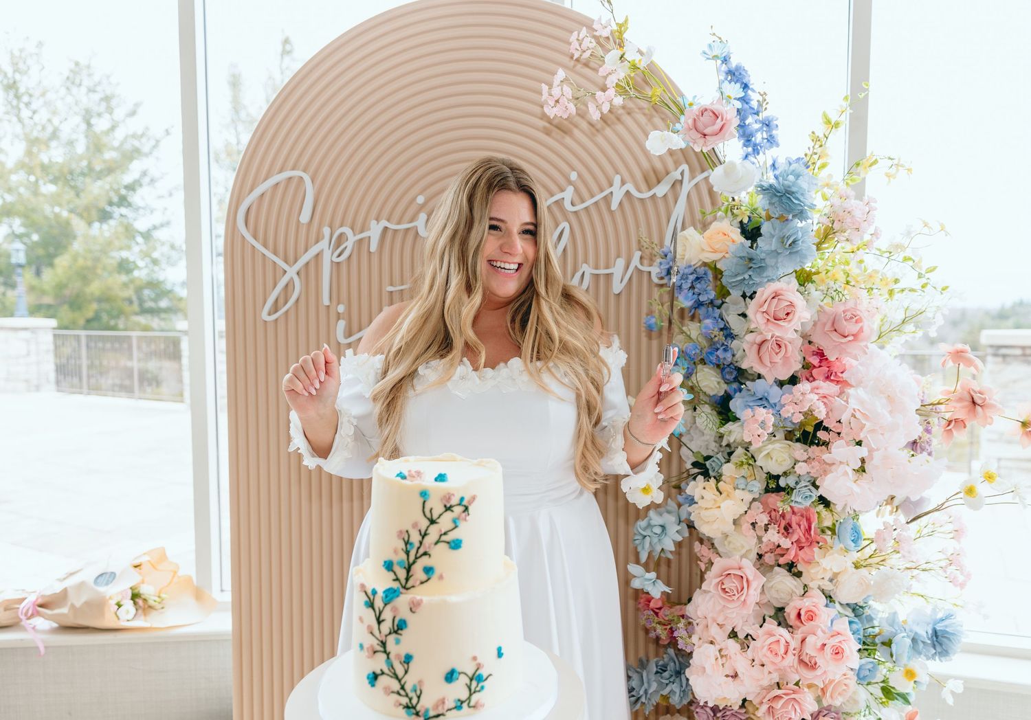 Elegant white cake with turquoise floral accents photographed in a light-filled room.