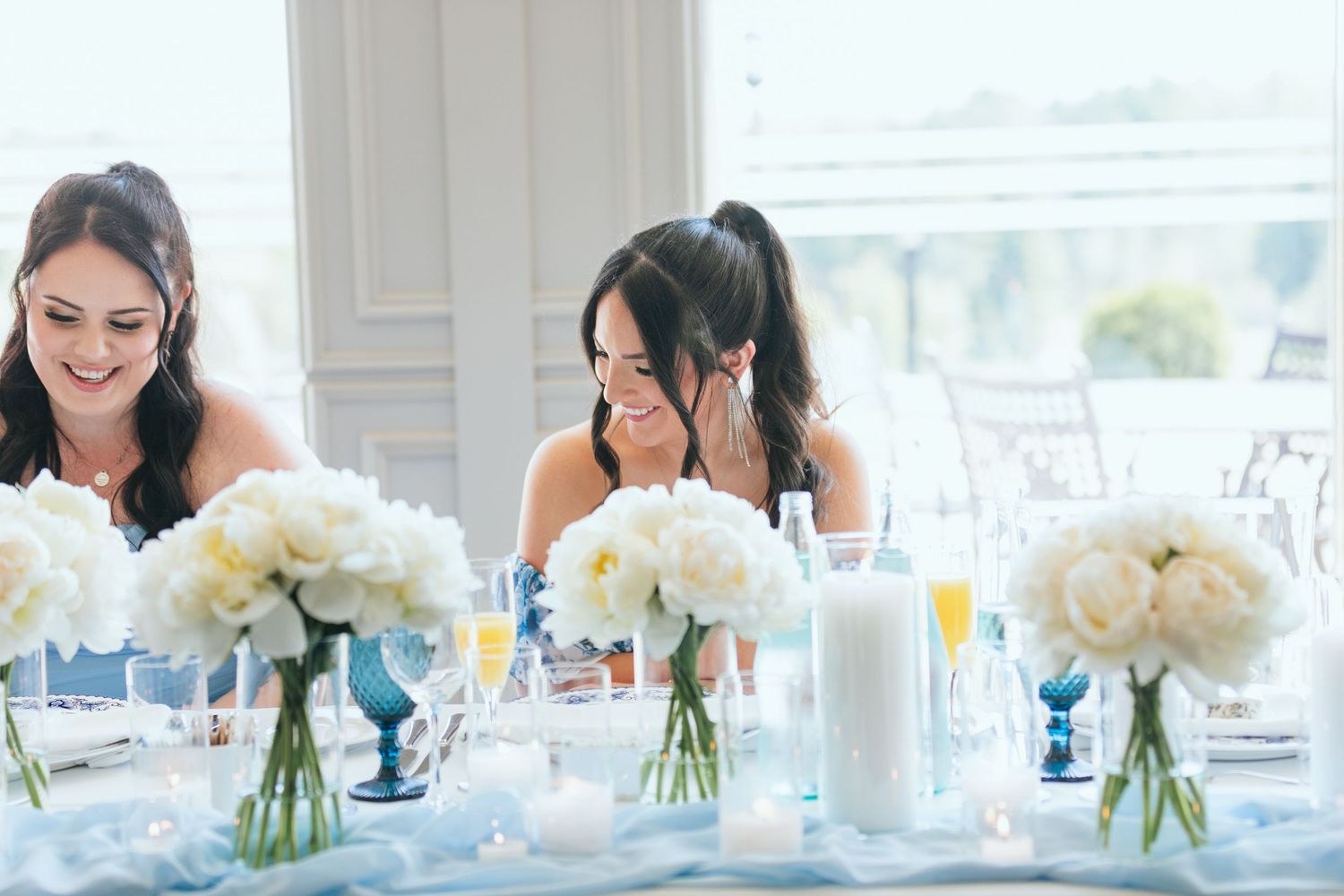 White floral centerpieces in glass vases arranged along a table with blue accents.