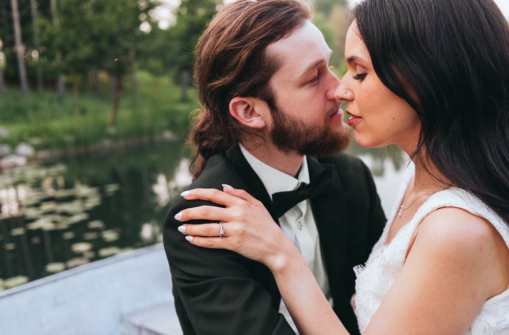 Intimate moment between bride and groom near a tranquil pond during their wedding photoshoot.