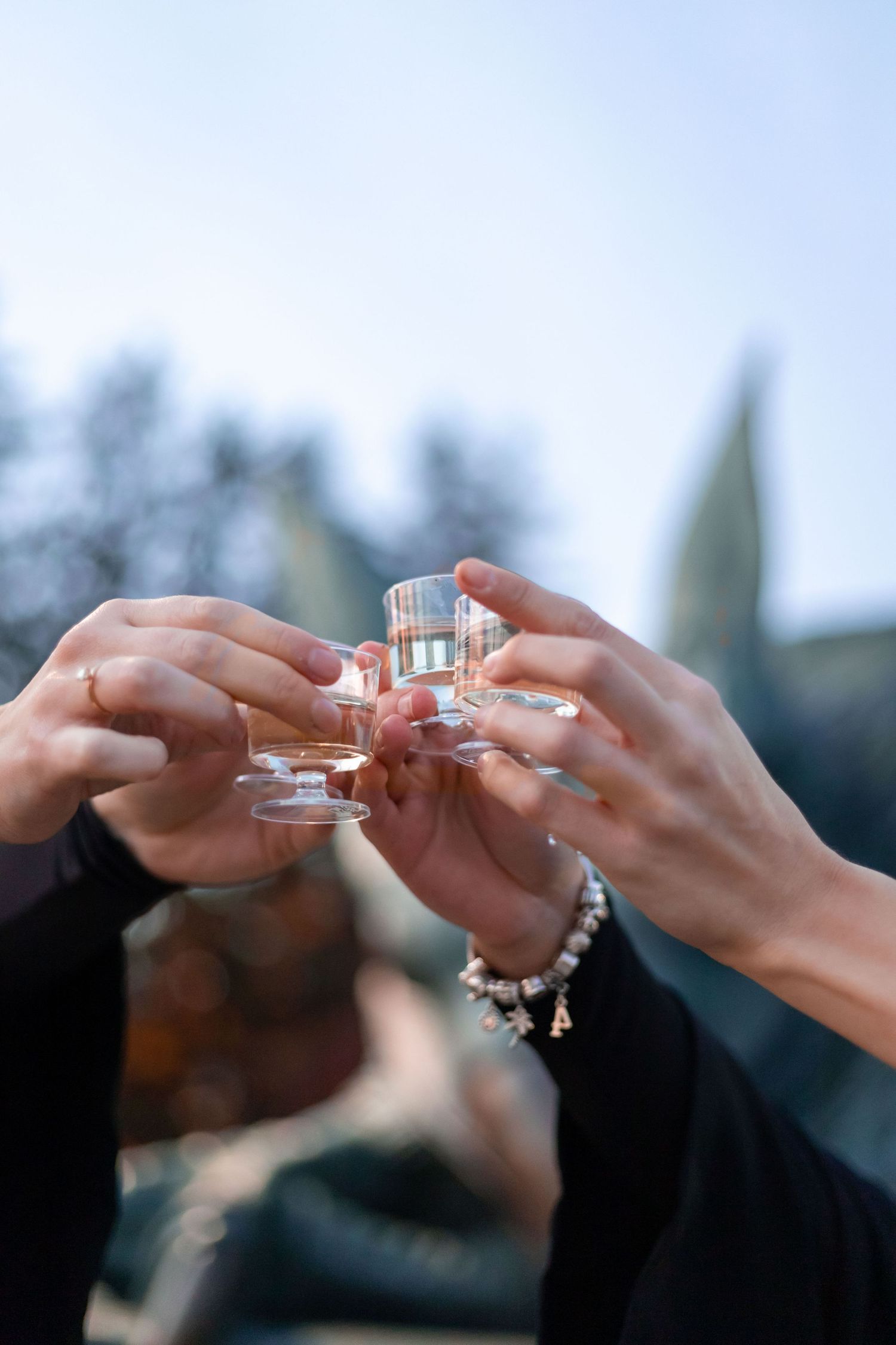 Hands clinking shot glasses together in an outdoor celebration.