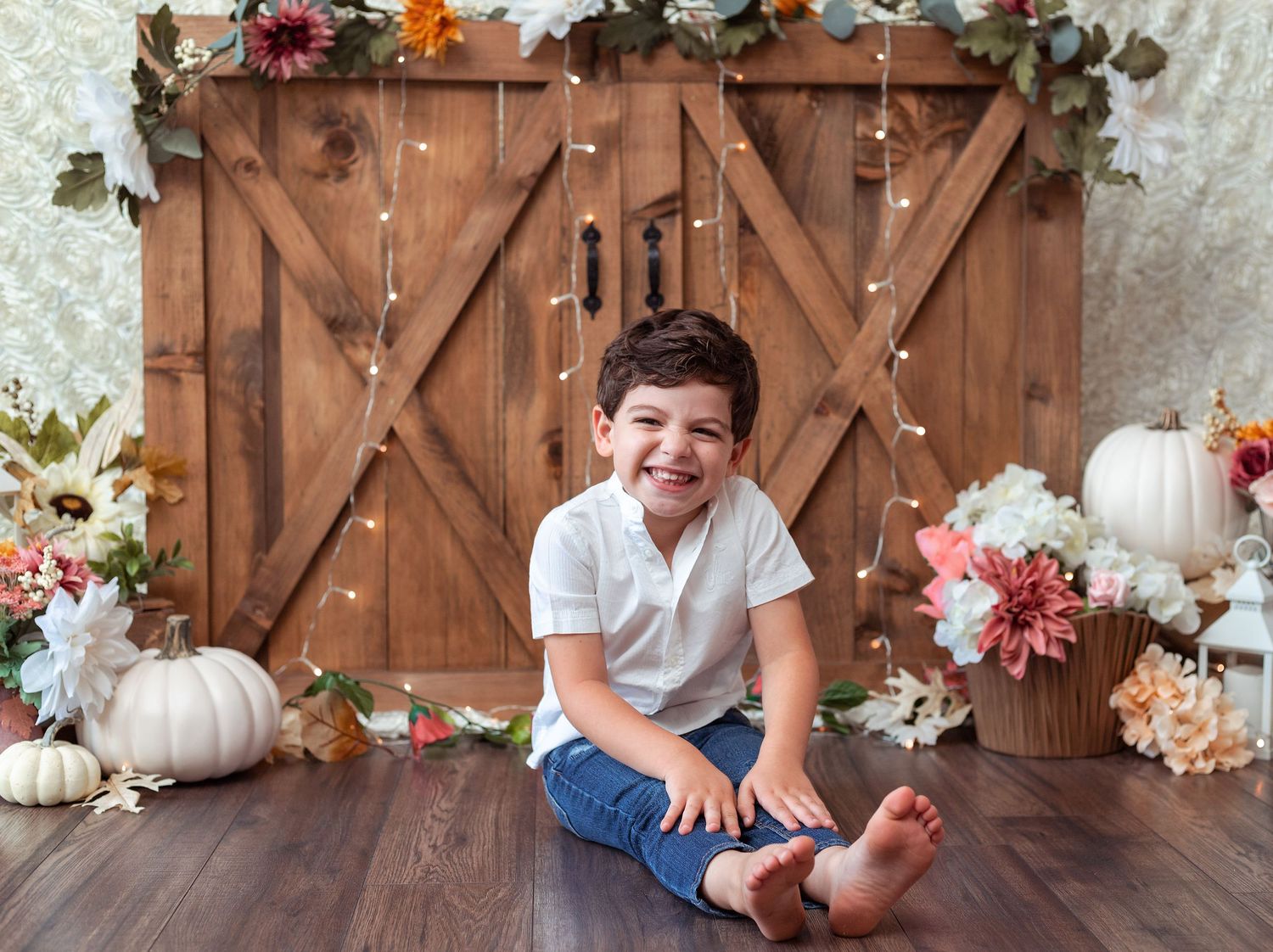 Rustic fall photo backdrop with wooden barn doors and autumn floral decorations.
