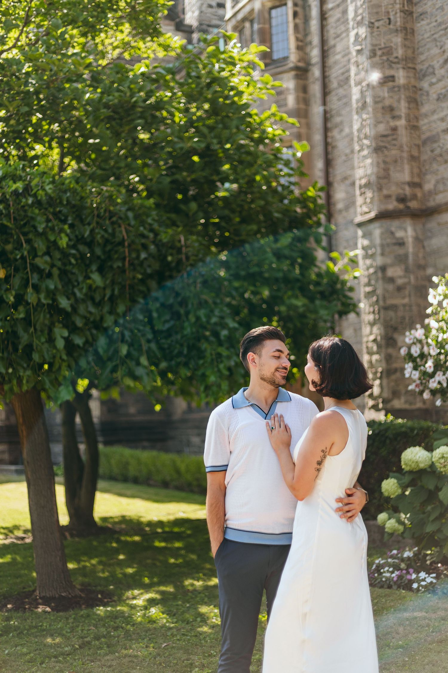 Summer garden photoshoot with couple in white against lush green backdrop.