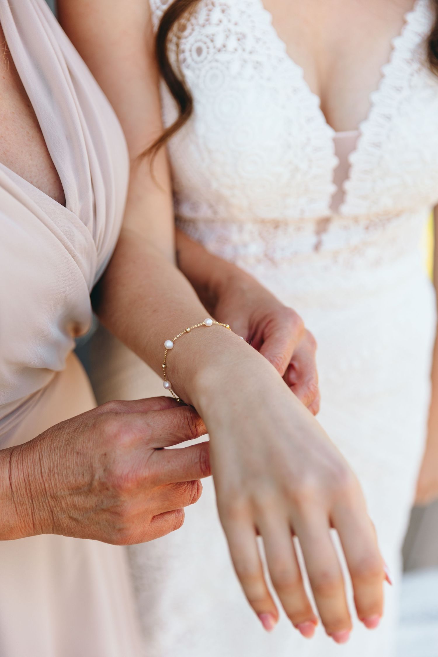 Close-up detail of hands adjusting delicate jewelry against white lace fabric.