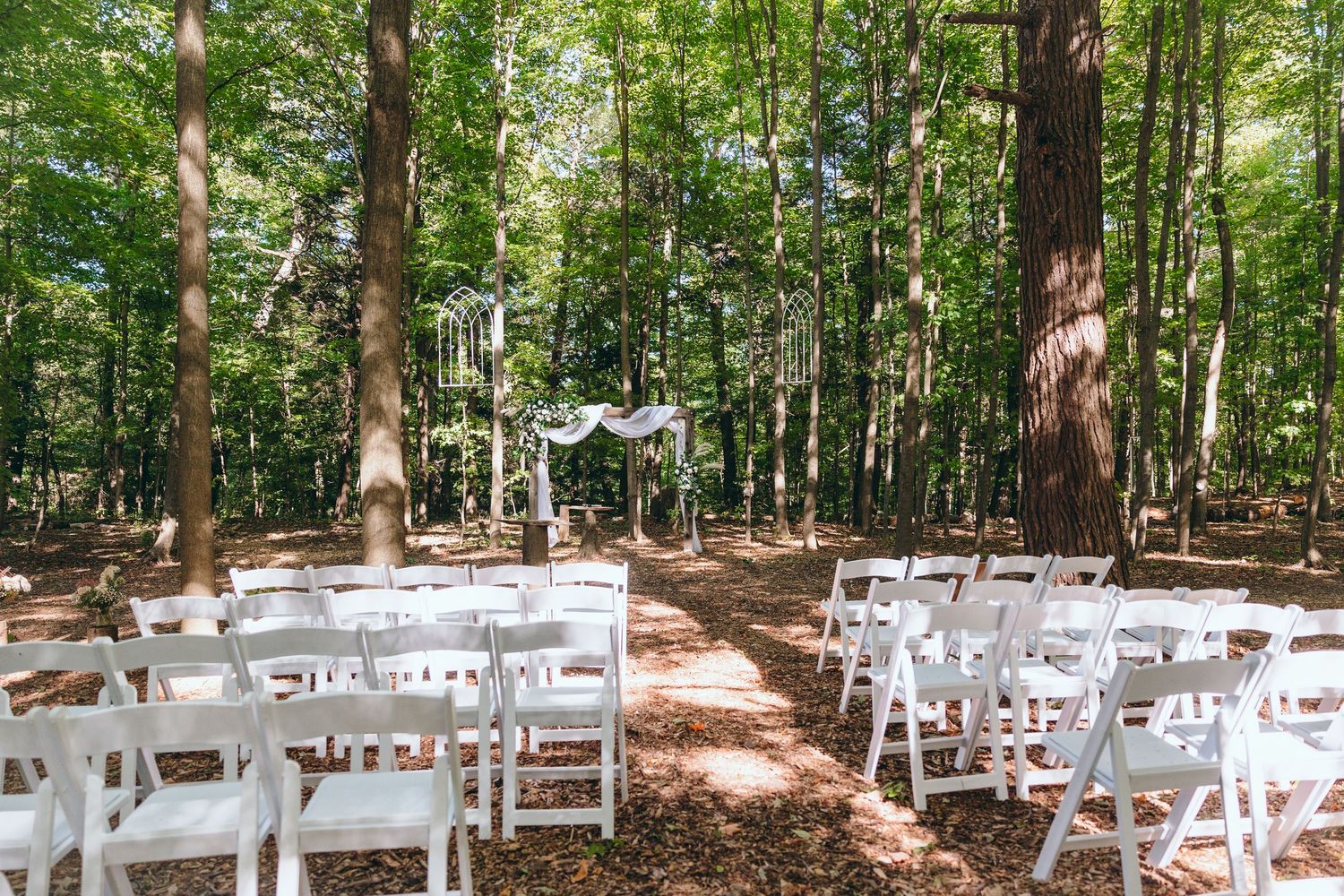 White chairs arranged in rows for an outdoor woodland wedding ceremony.