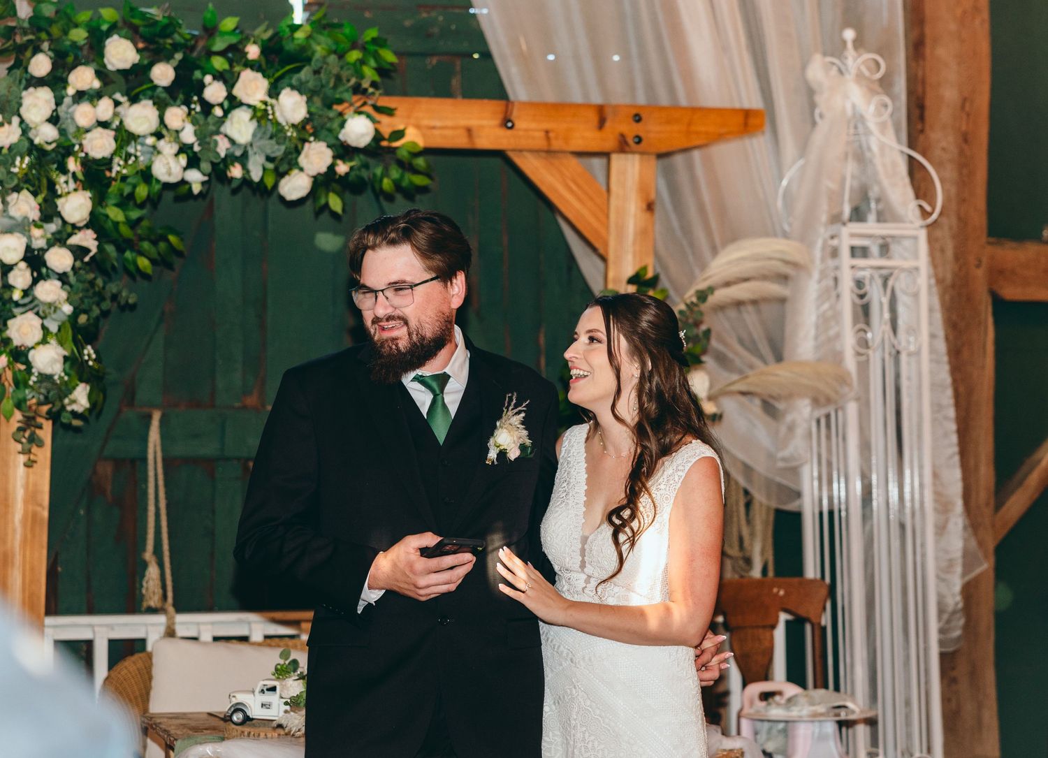 Couple shares intimate moment during reception with floral decor and wooden beams.