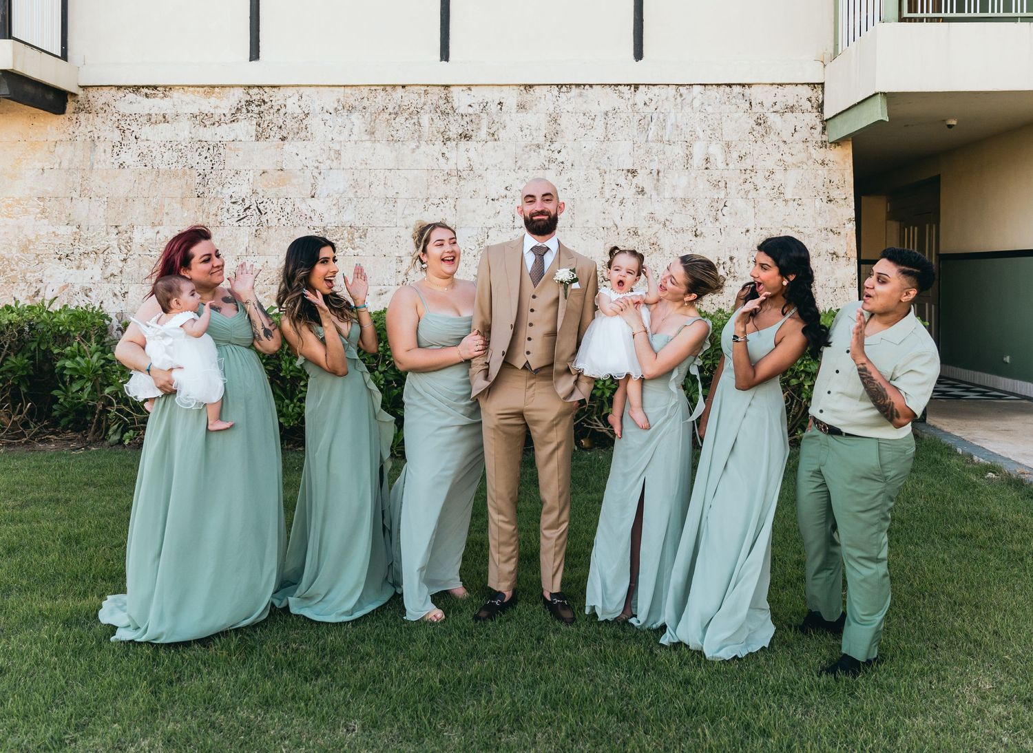 Wedding party in mint green dresses and formal attire poses together on grass.