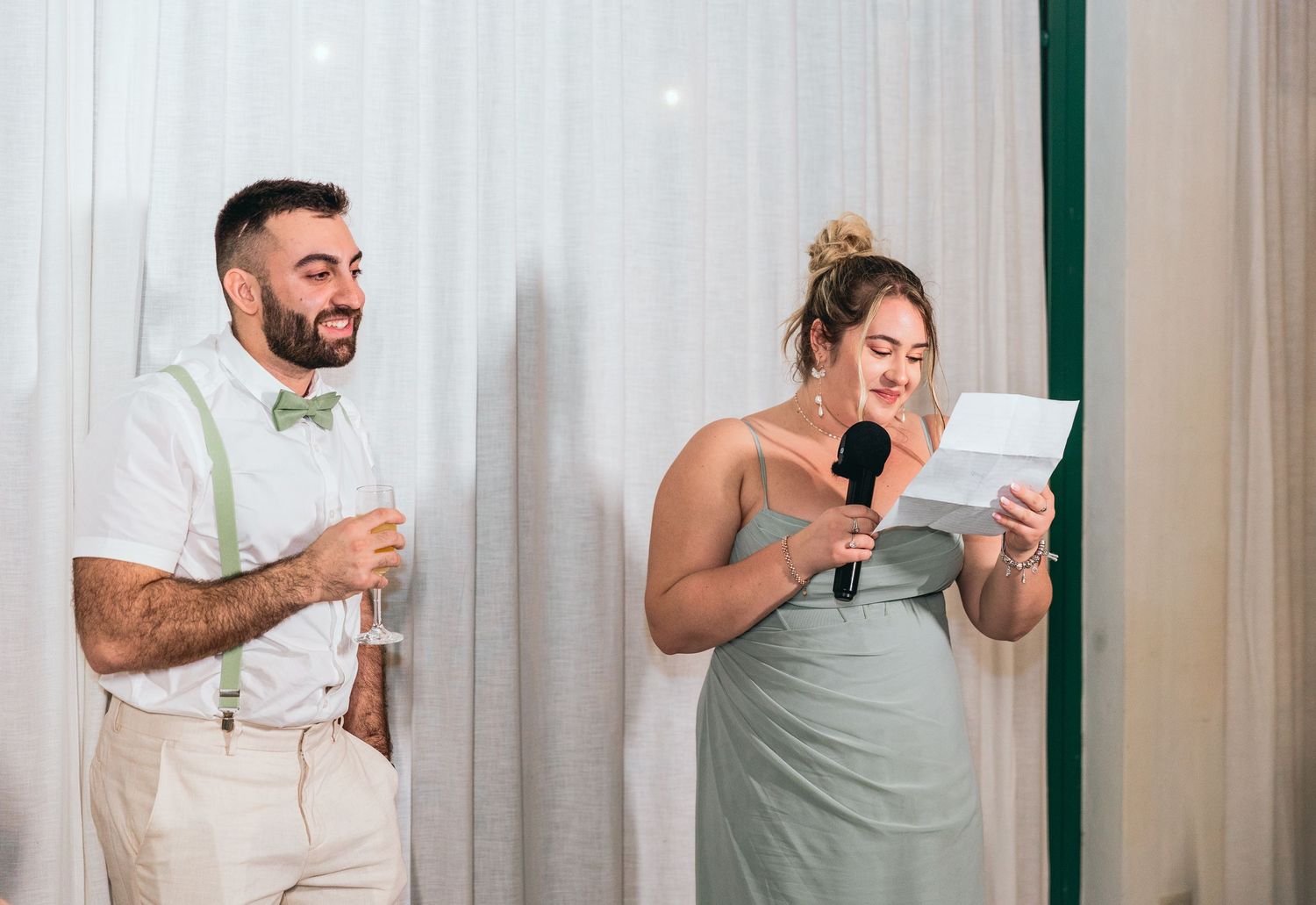 Wedding party members in sage green and white attire give emotional speeches at reception.