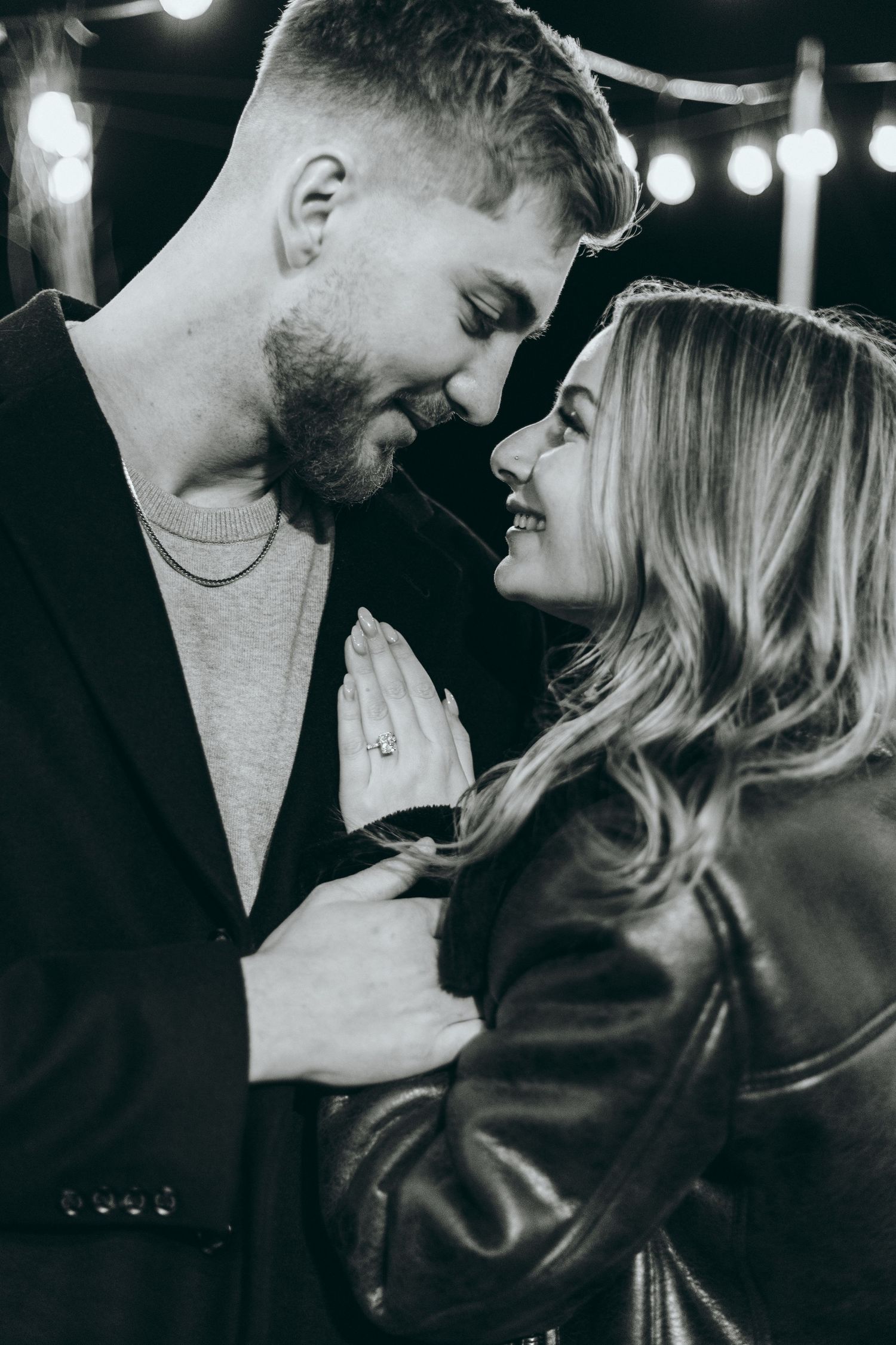 A romantic black and white photo of a couple sharing an intimate moment under string lights.