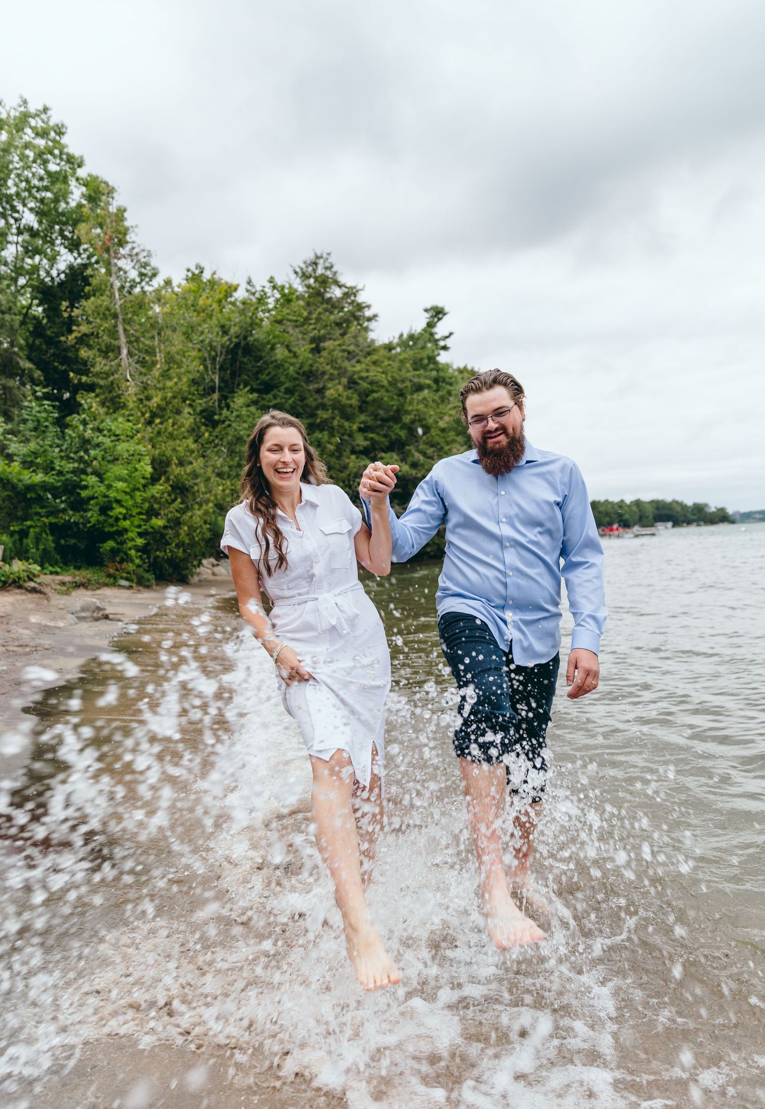 Joyful couple splashing water at beach shore during cloudy day.