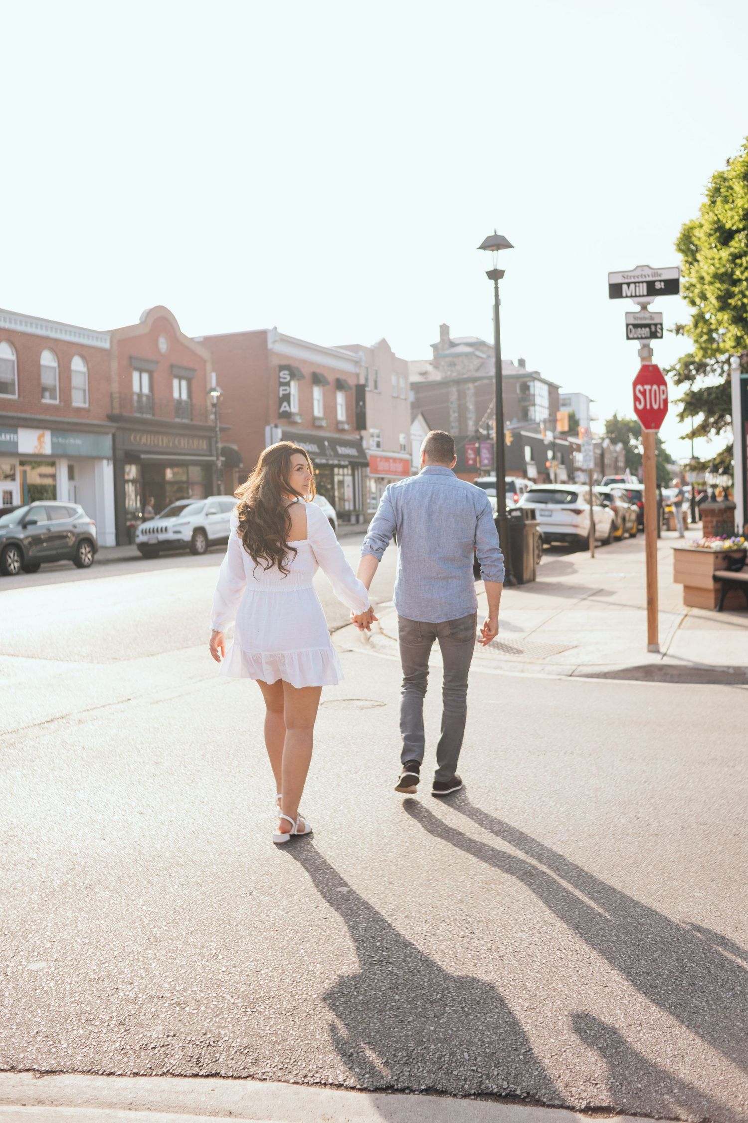Couple walking down a sunny urban street casting long shadows.