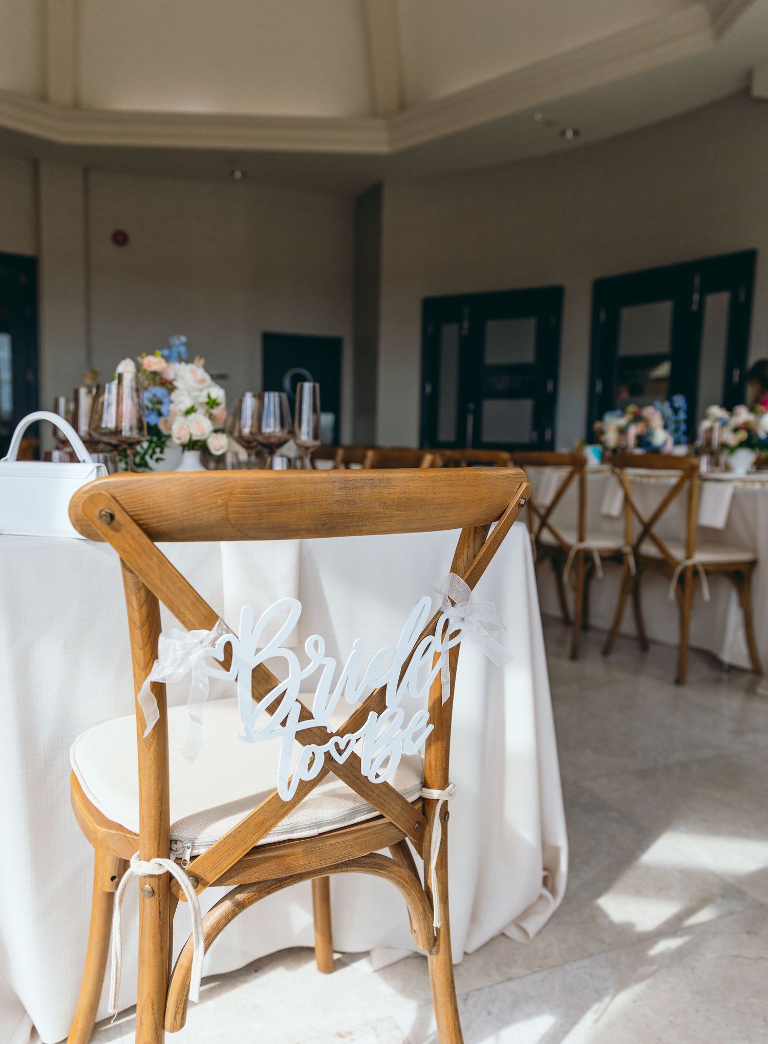 White reception space with wooden cross-back chairs and elegant text decorations on the seats.