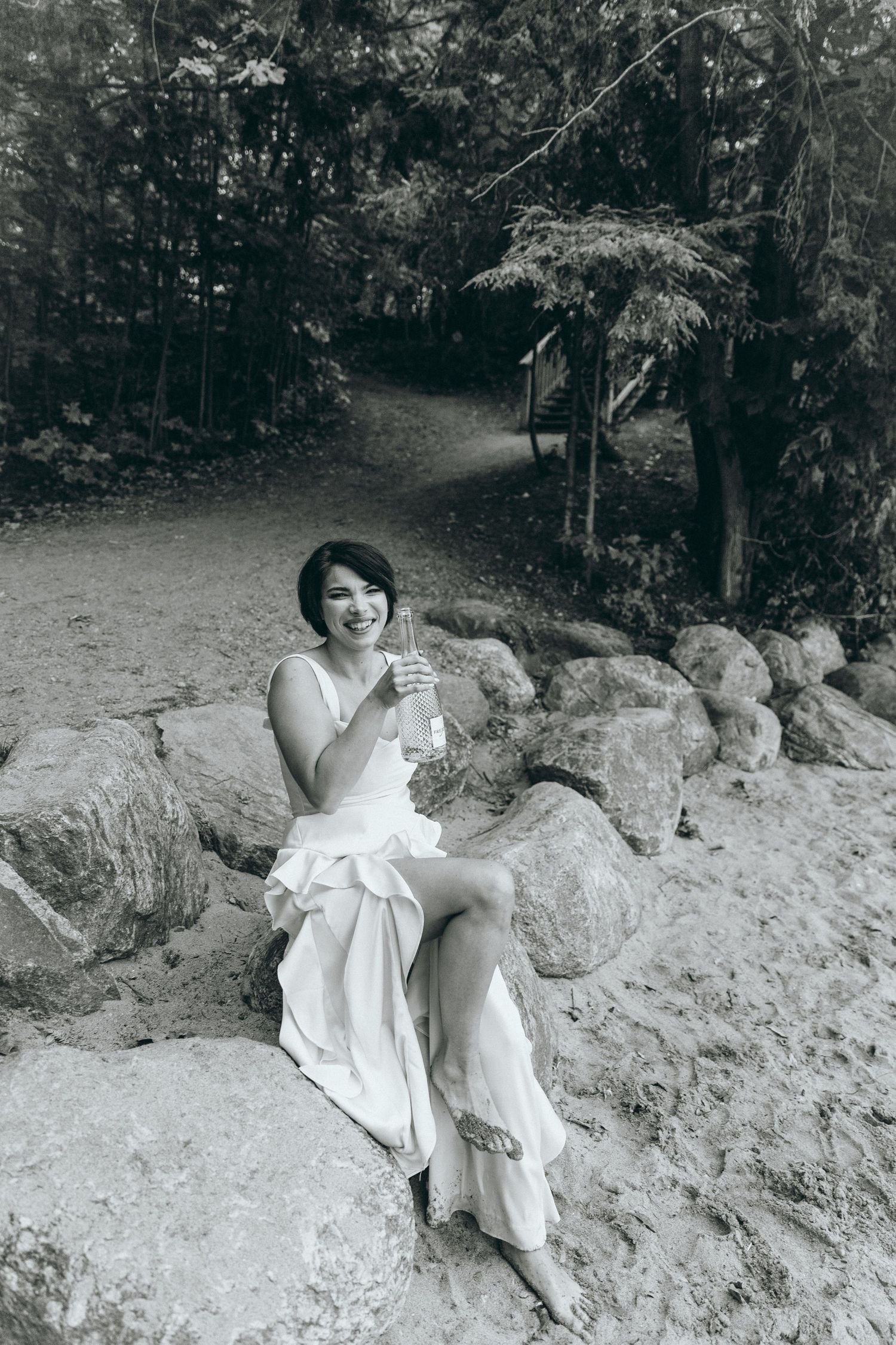 Person in white dress sits on rocky shoreline during outdoor photo session.