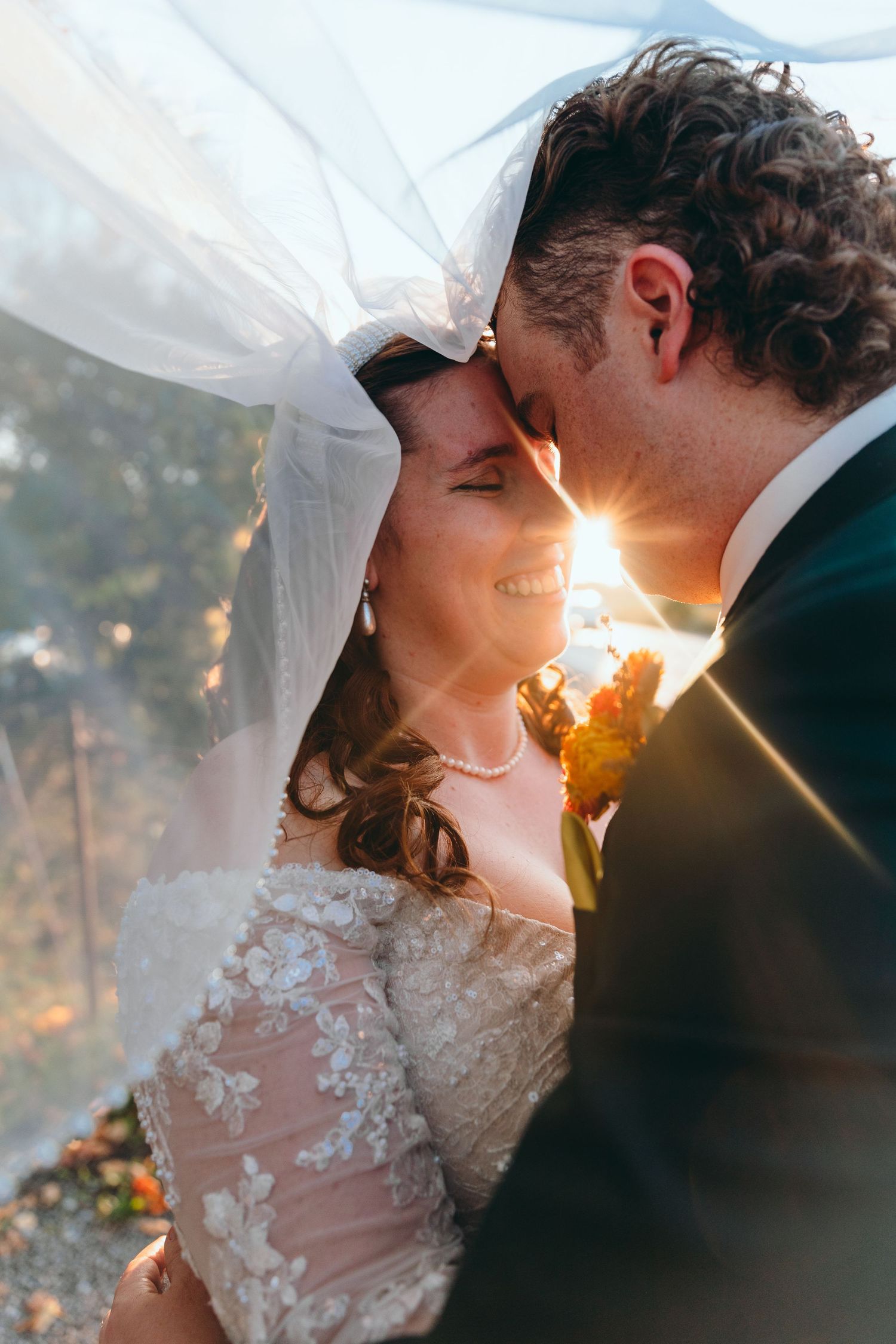 Ethereal wedding portrait with sunlight streaming through white veil during intimate moment.