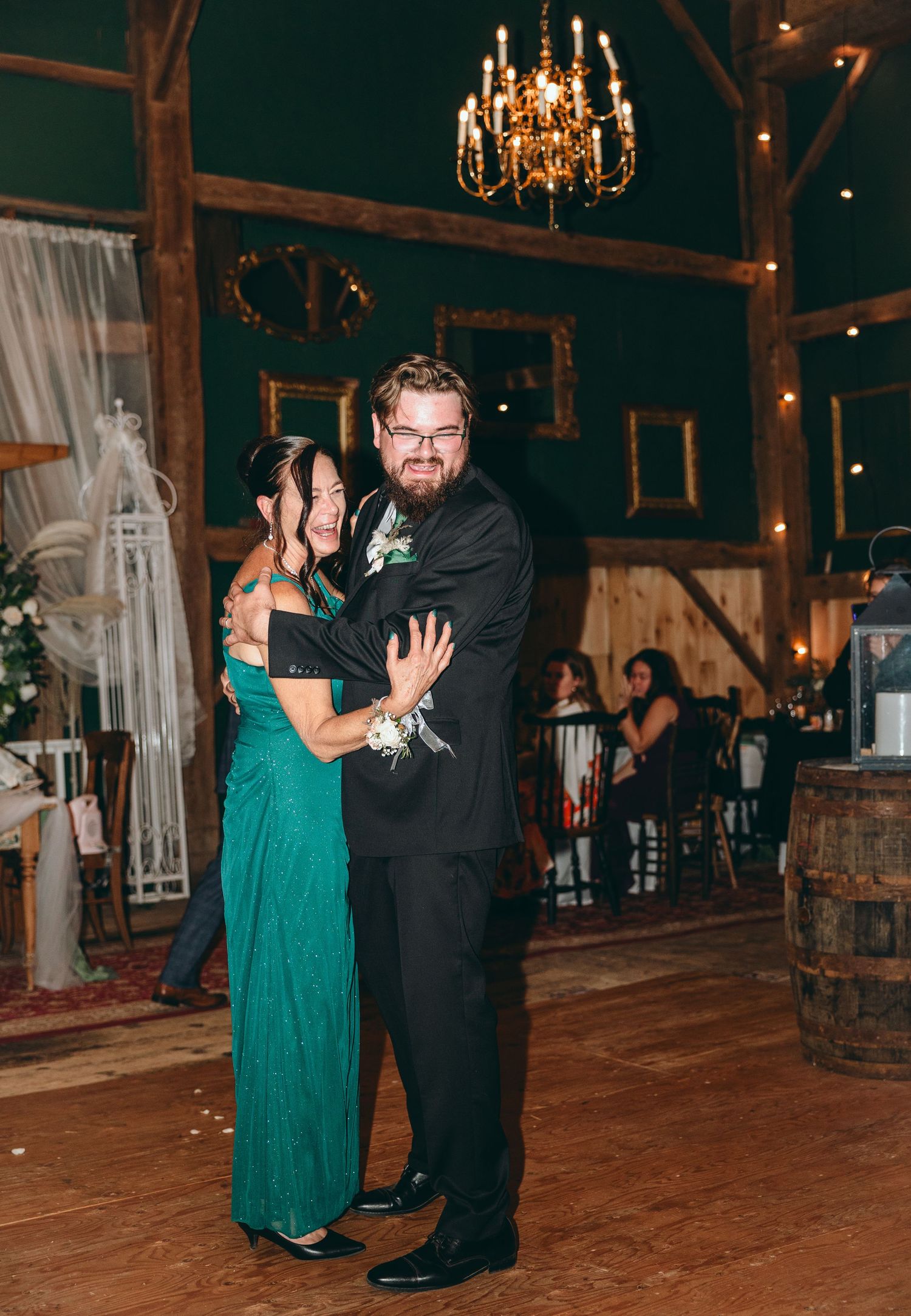 Couple dancing in formal attire at a rustic barn wedding reception with chandelier lighting.