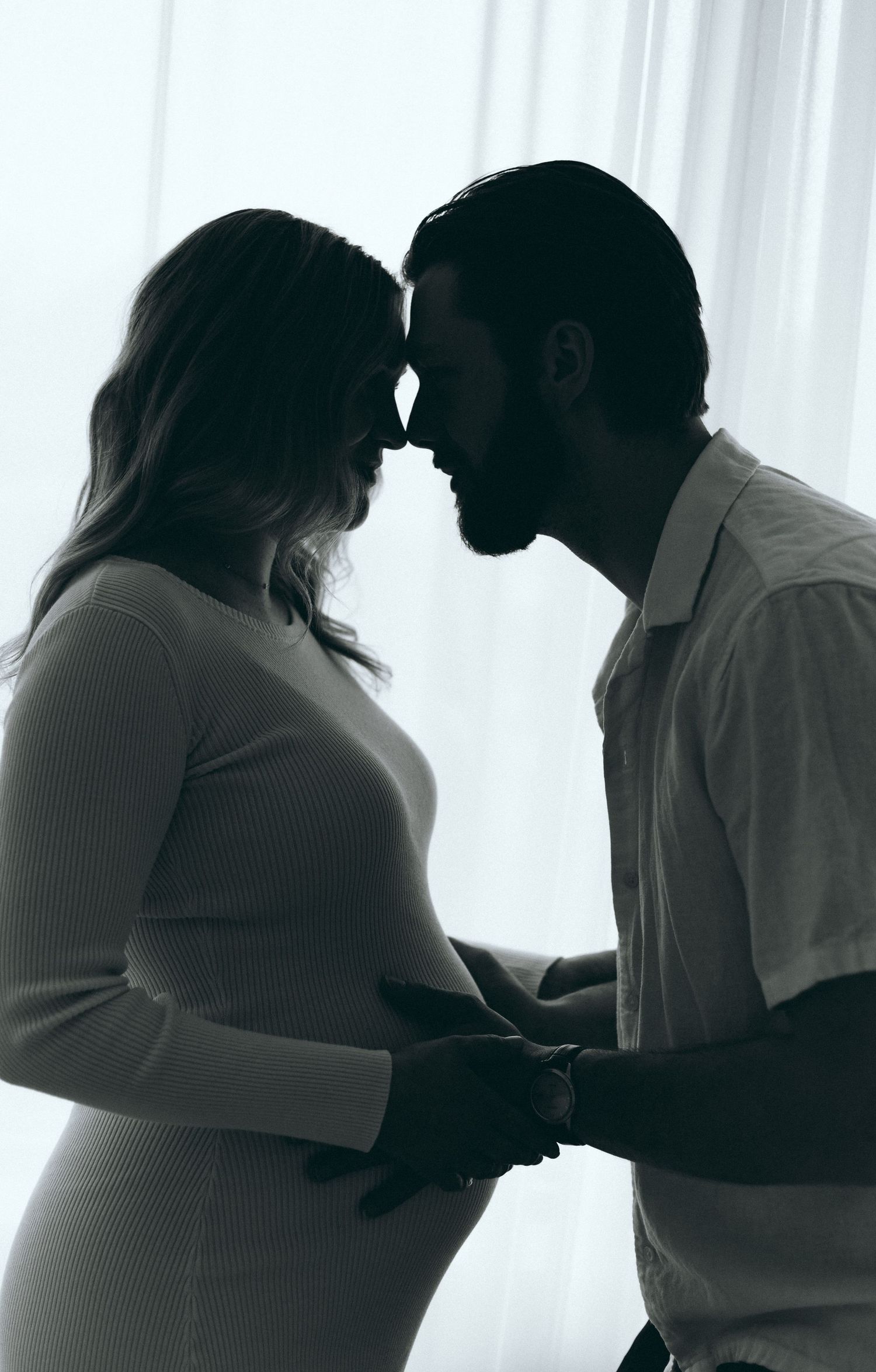 Silhouetted maternity photos showing intimate moments between couple by window.