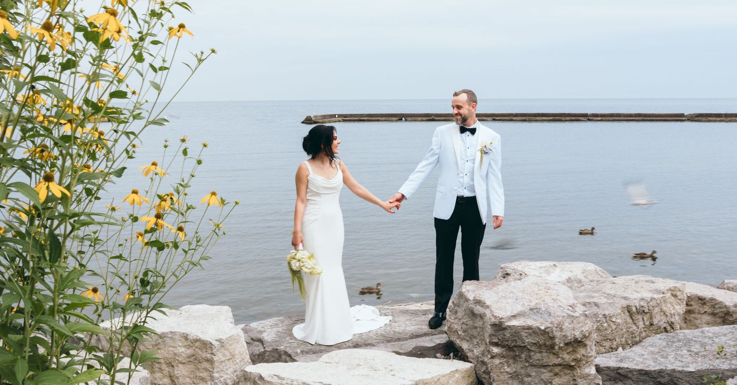 Wedding couple shares romantic moments on rocky beach with yellow wildflowers nearby.