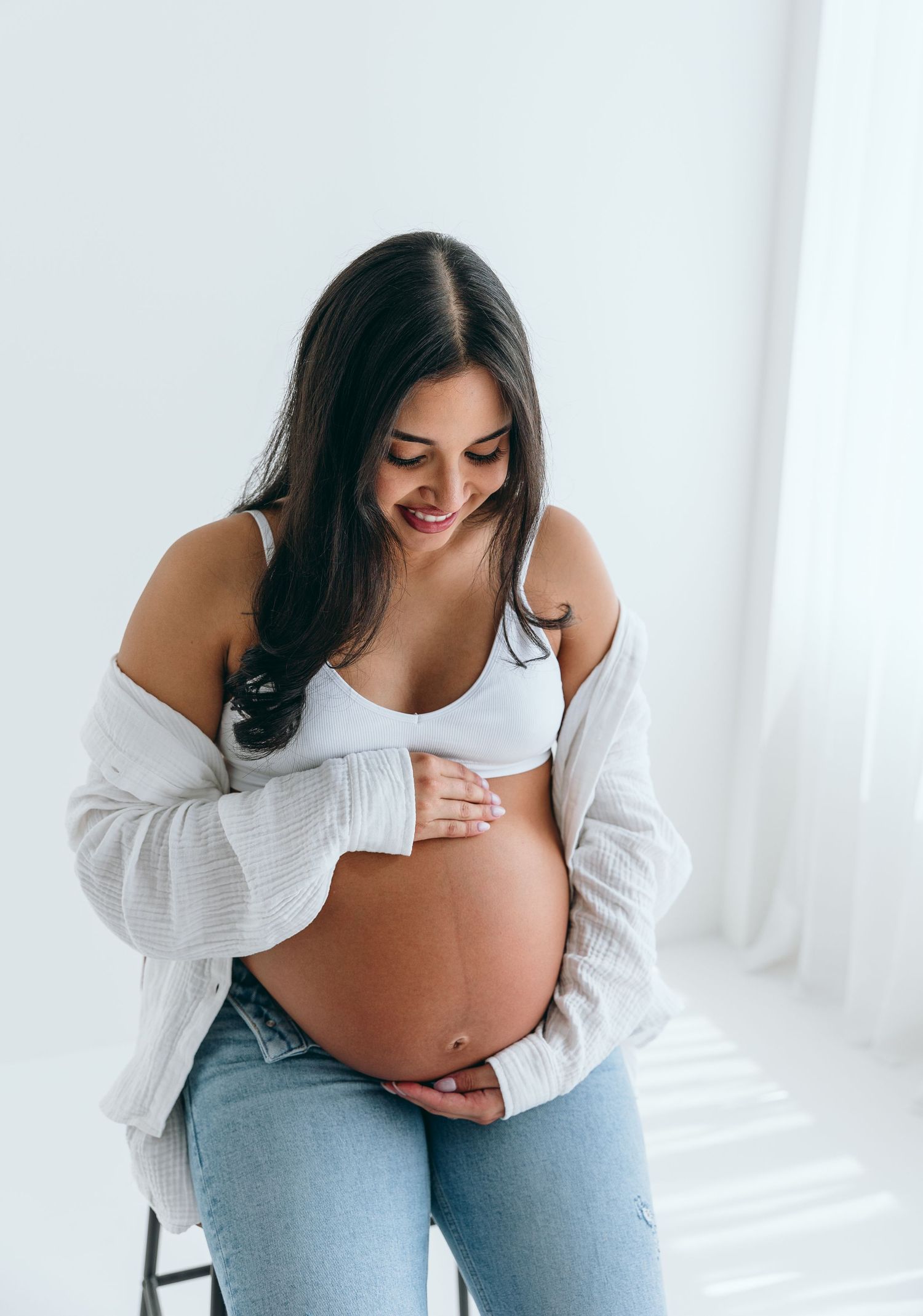 Candid maternity photo showing pregnant belly in white studio setting.