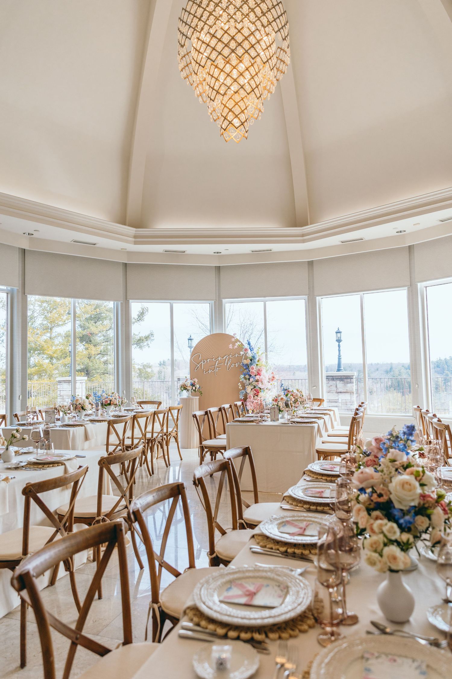 Bright sunlit reception venue with cross-back chairs and elegant table settings in a panoramic room.