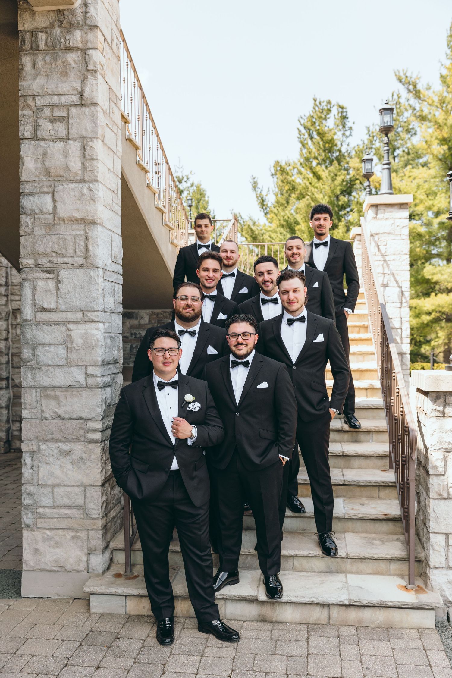 Groomsmen in black tuxedos descend stone staircase during wedding celebration.