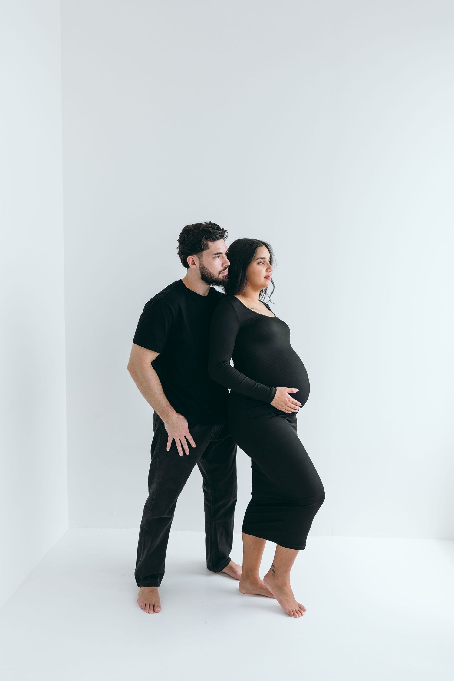 Artistic maternity photoshoot series showing couple in black outfits against white backdrop.