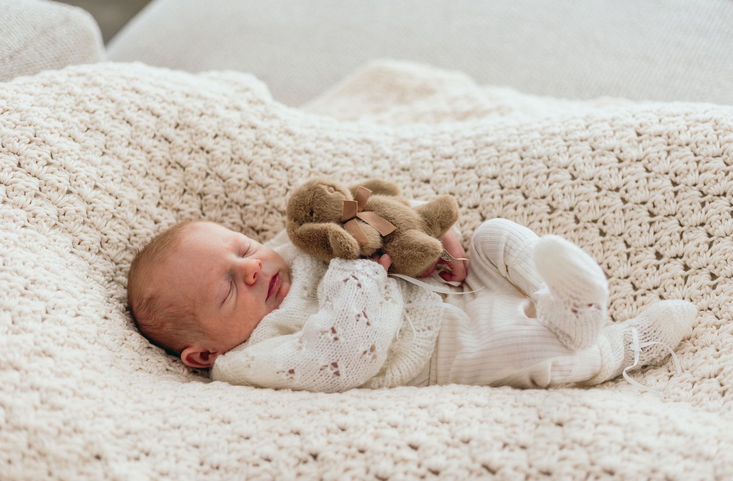 Baby in white onesie resting on textured cream blanket.