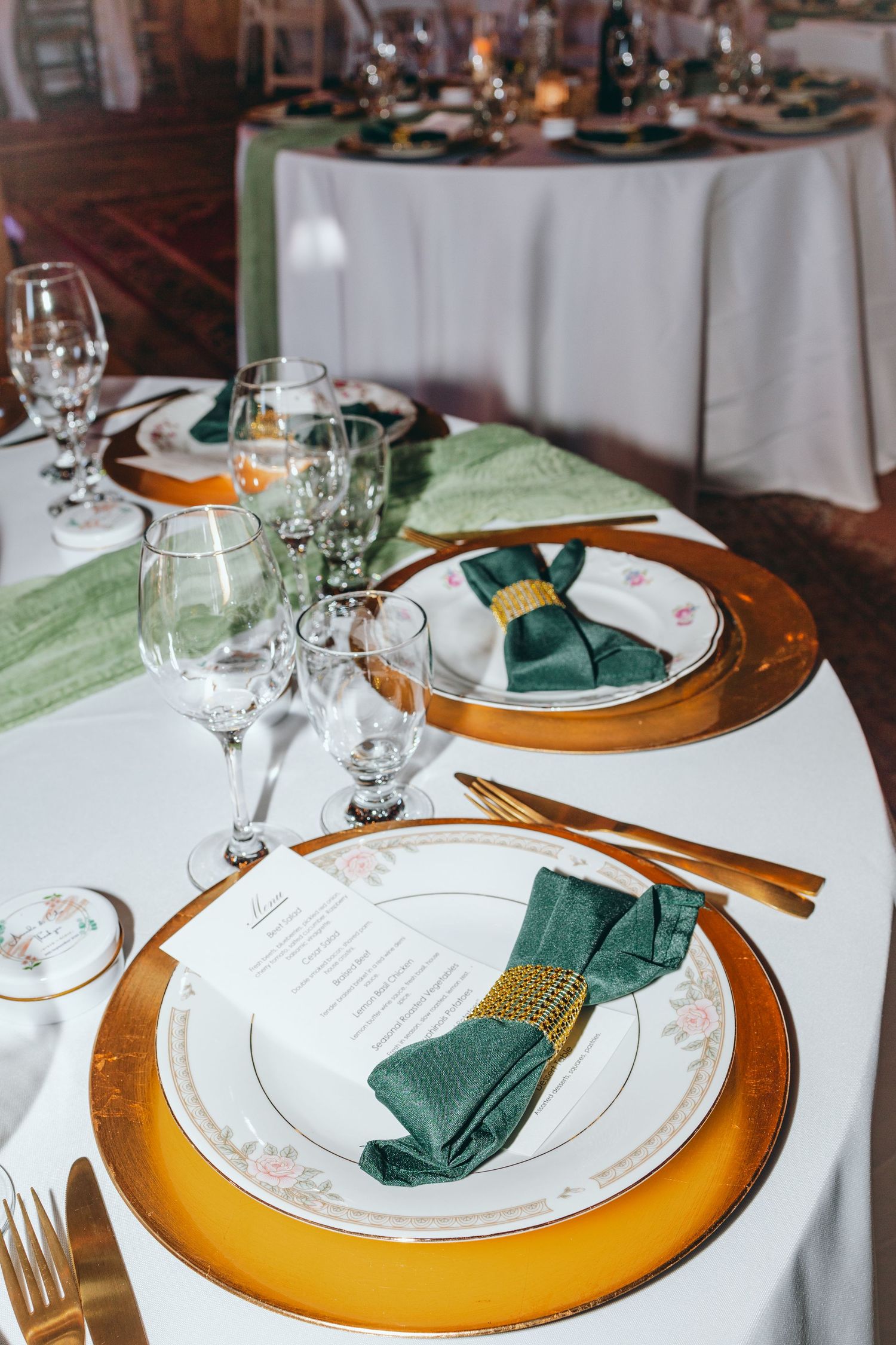 Elegant table settings with gold chargers, white plates and emerald green napkins.