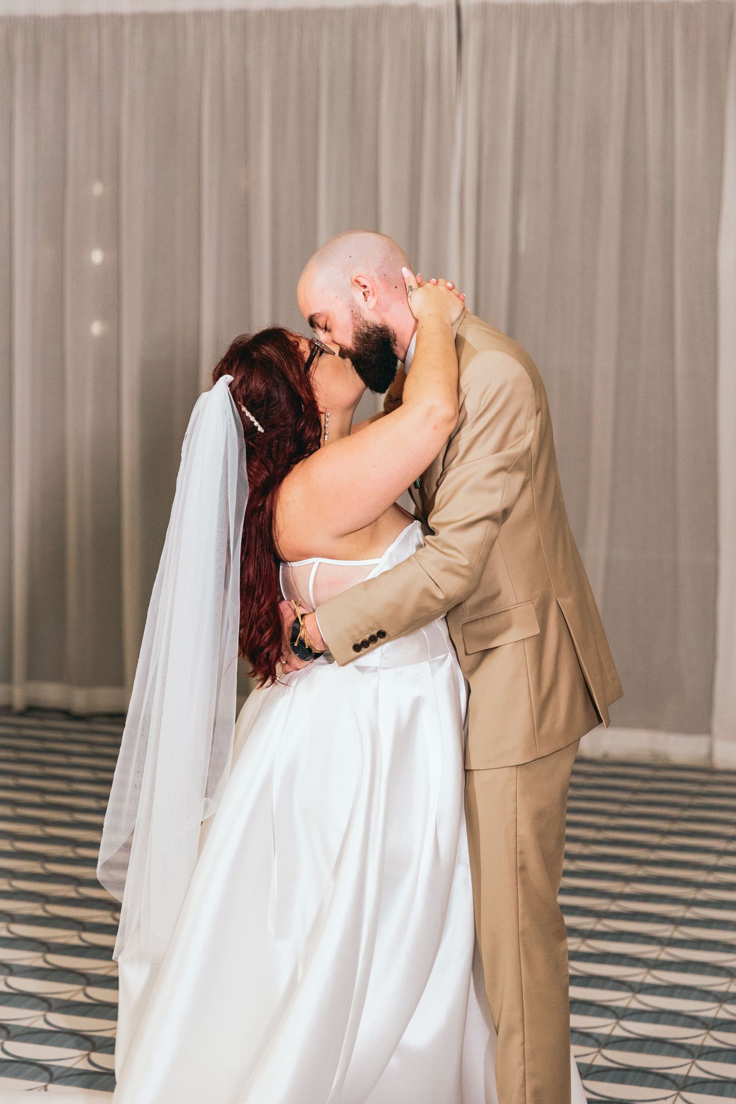 Romantic first dance moment between newlyweds on a geometric patterned dance floor.