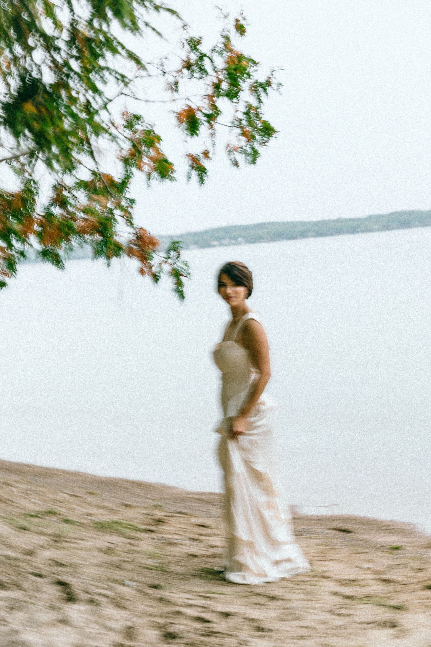 Ethereal beach photoshoot with flowing white dress against water backdrop.