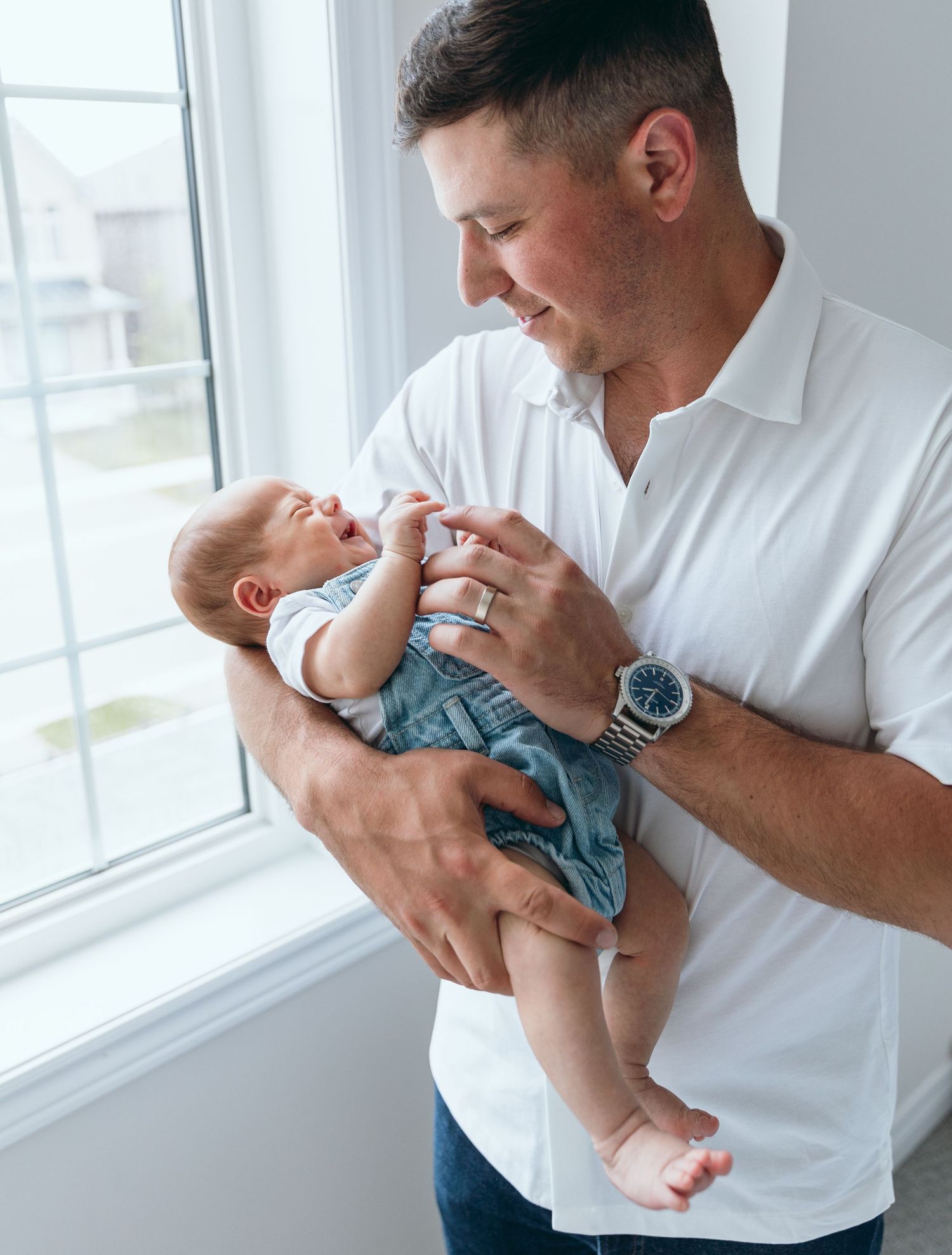 An adult in a white shirt holds and plays with a baby wearing blue.