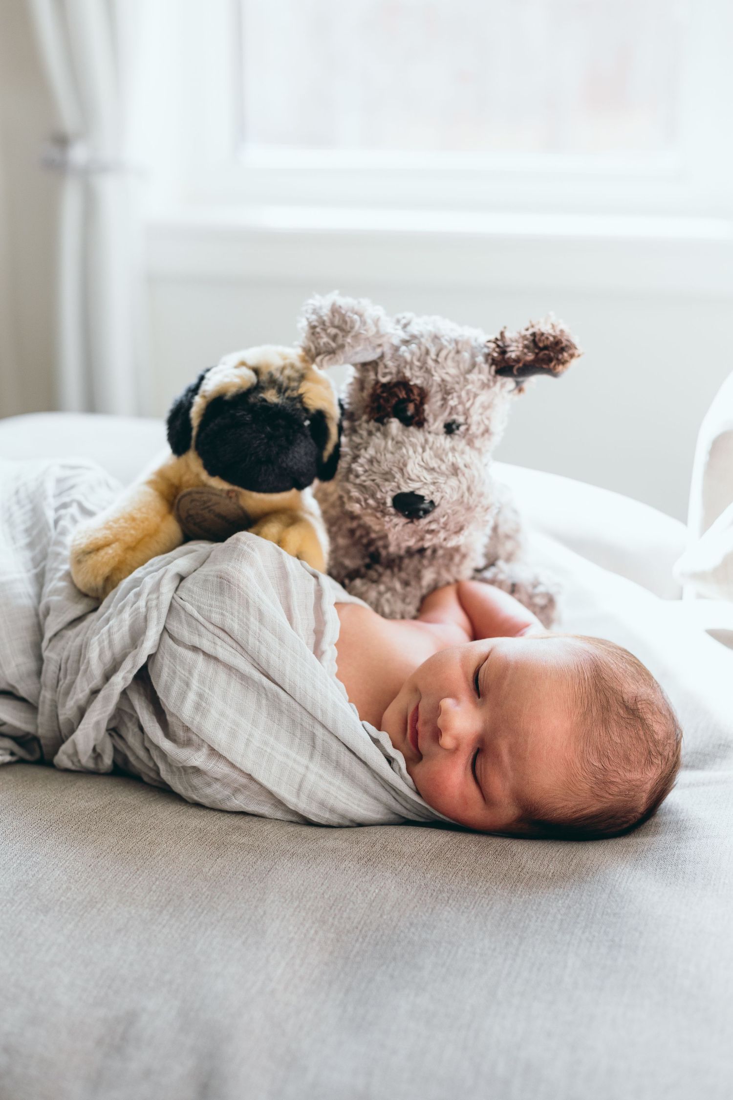 Newborn baby lying on white surface with stuffed animal toys.