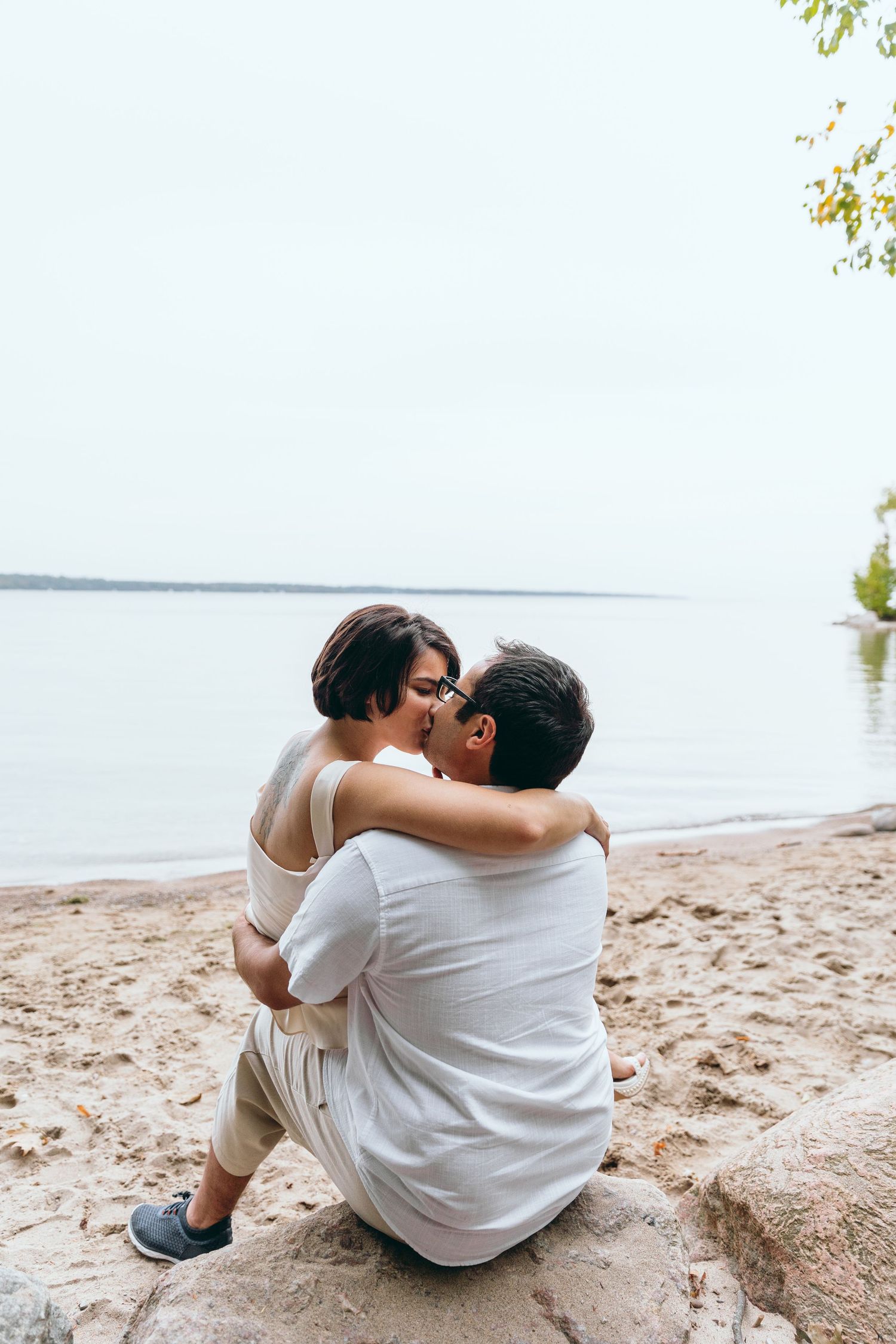Couple sitting together on a sandy beach overlooking calm waters.