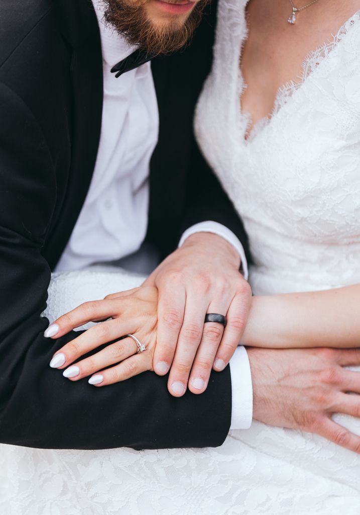 Close-up of newlyweds' hands showing their wedding rings against formal attire.