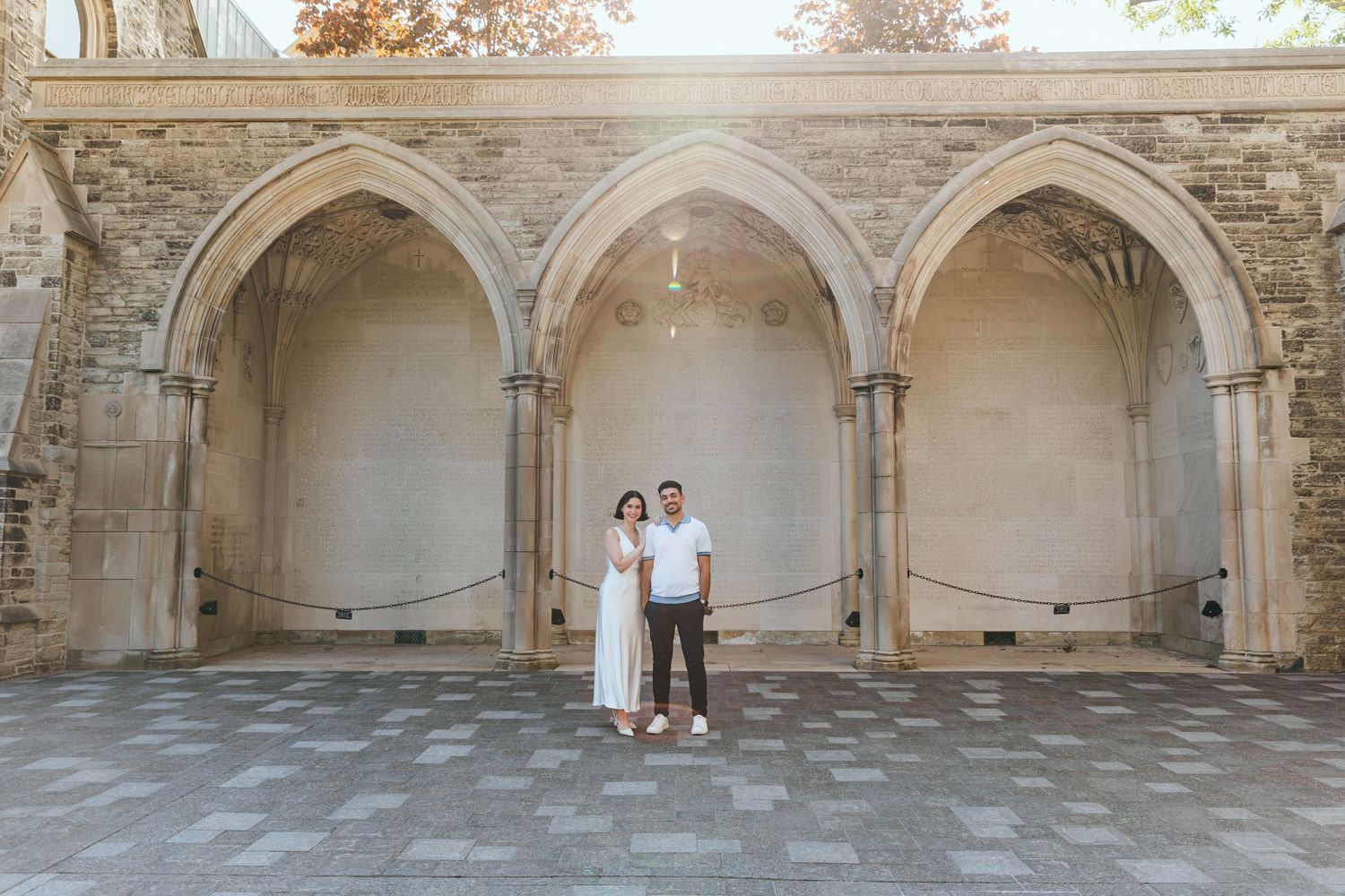 Romantic couple stands beneath gothic stone arches in a historic courtyard setting.