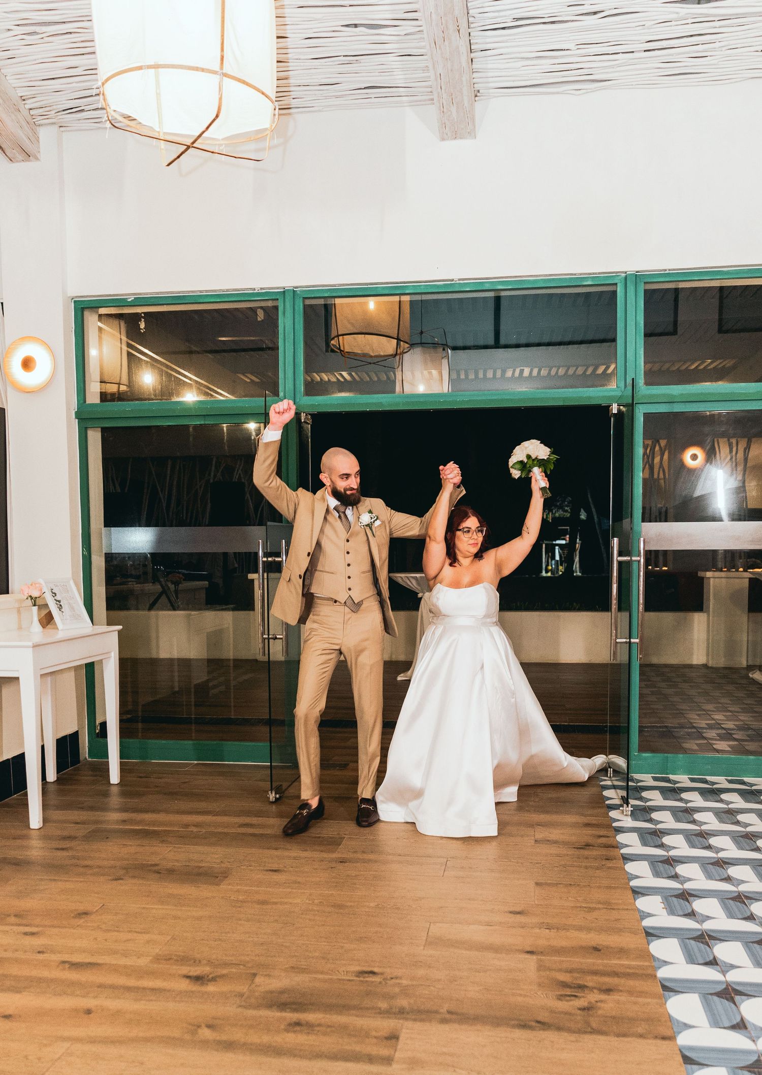 Wedding guests dance and celebrate in a modern venue with wooden floors and glass walls.
