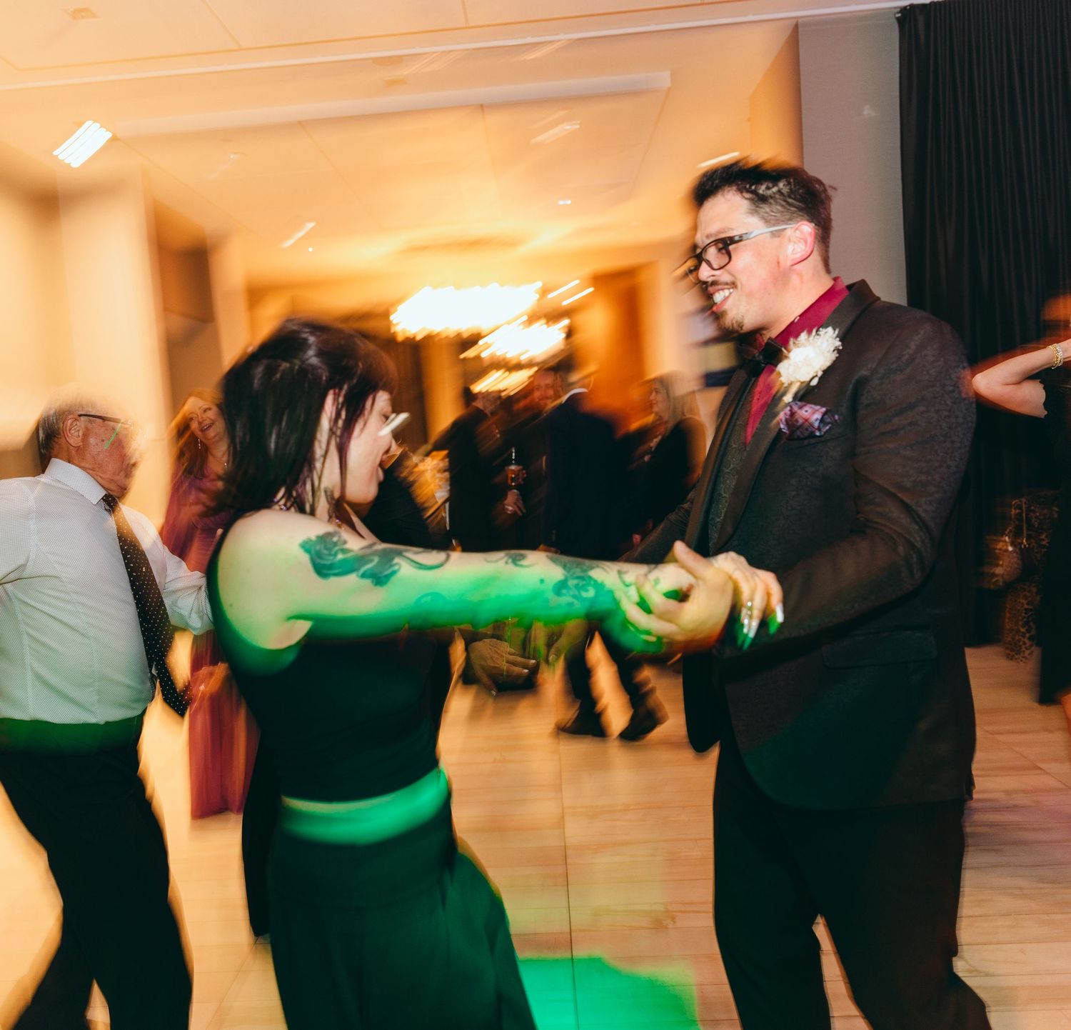Wedding guests dancing in a line at a reception with green lighting effects.