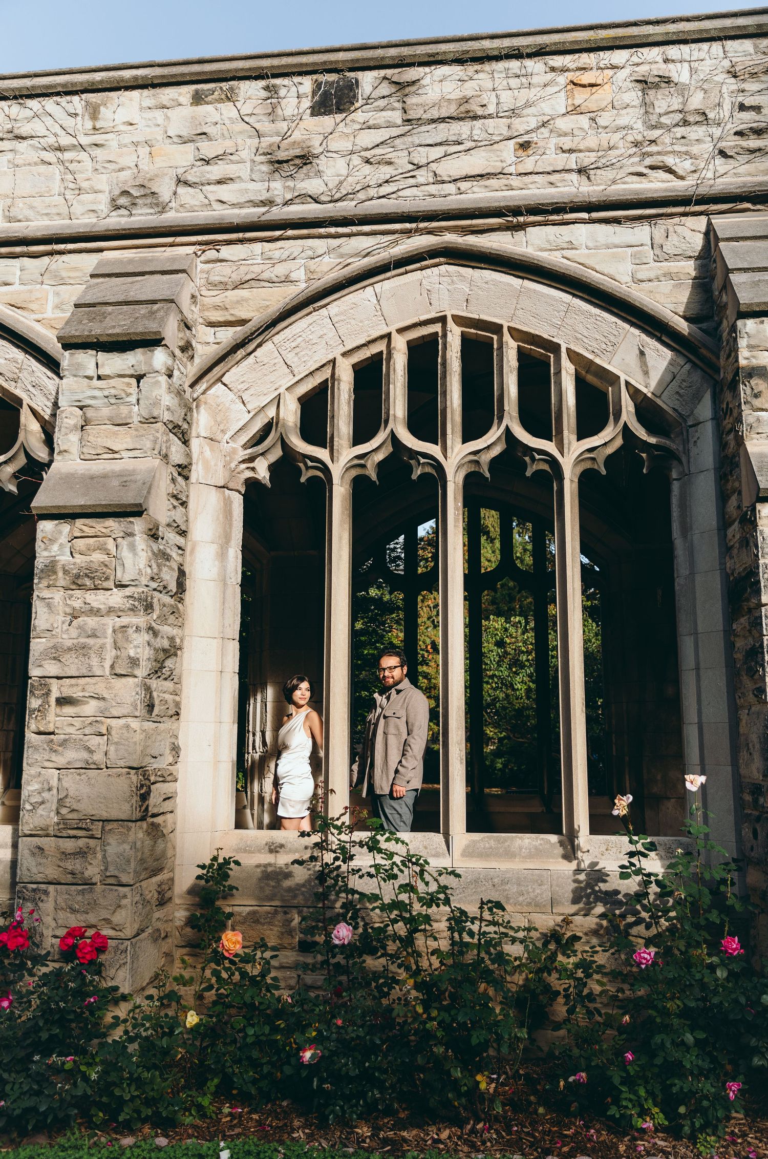 Gothic stone architecture with arched windows and blooming rose bushes in the foreground.
