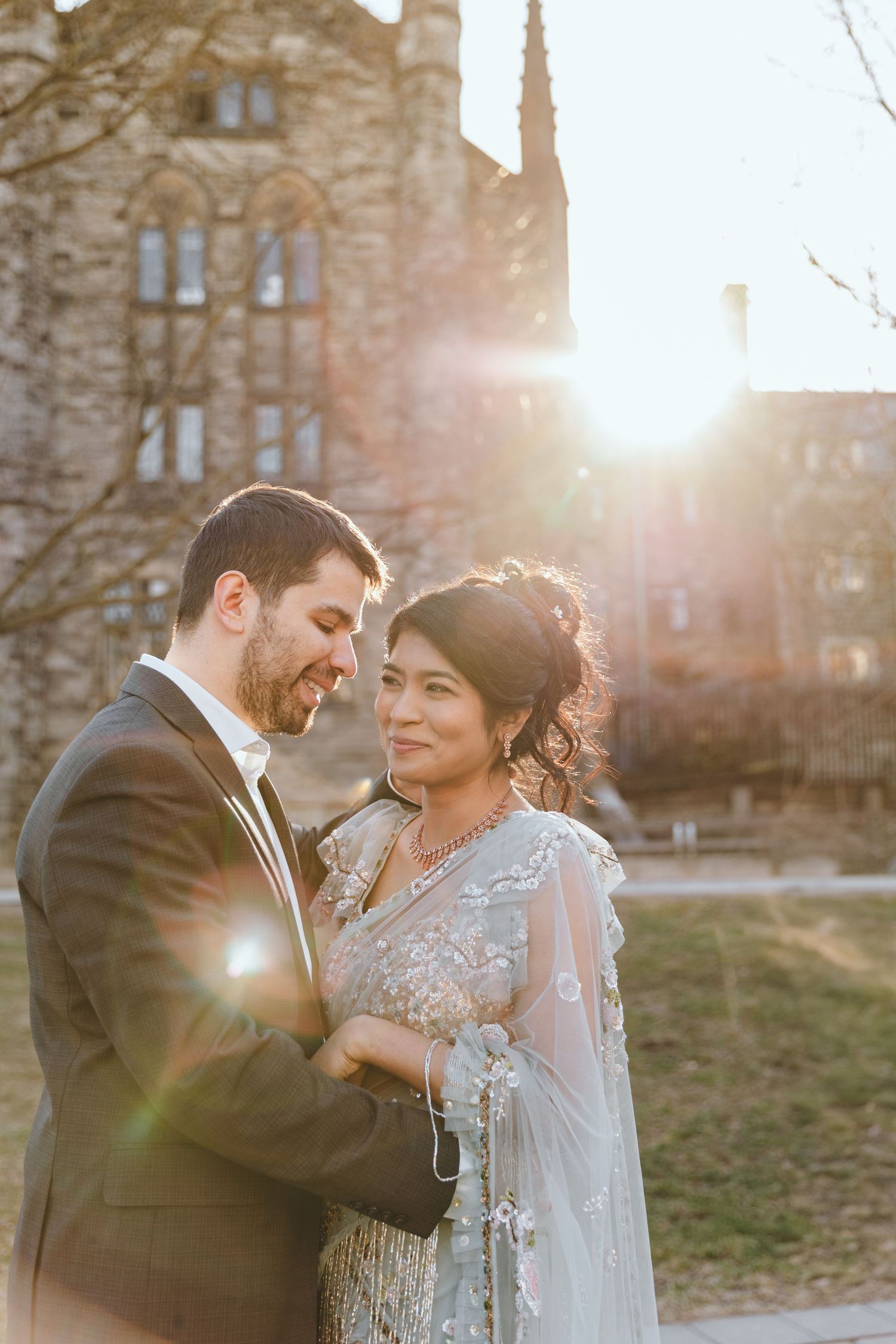 A couple shares an intimate moment in front of a historic stone building at sunset.