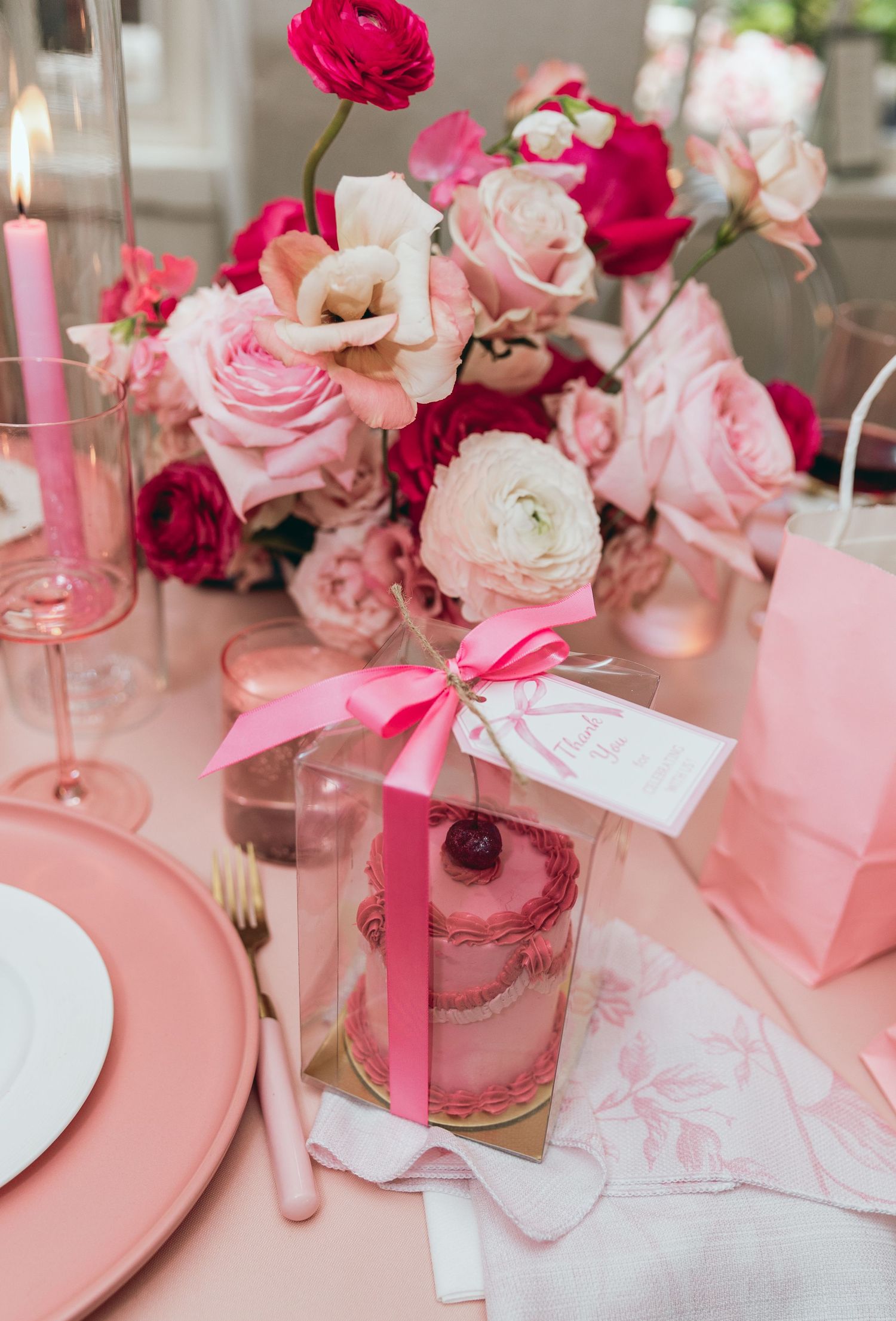 Pink and red floral centerpieces with white stationery and ribbons on a pastel pink tablecloth.