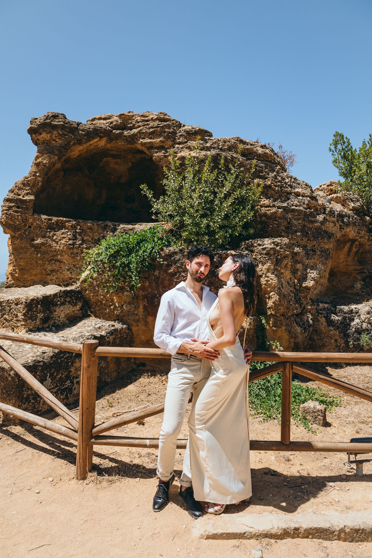A romantic photoshoot along a desert trail with rocky formations and wooden railings.