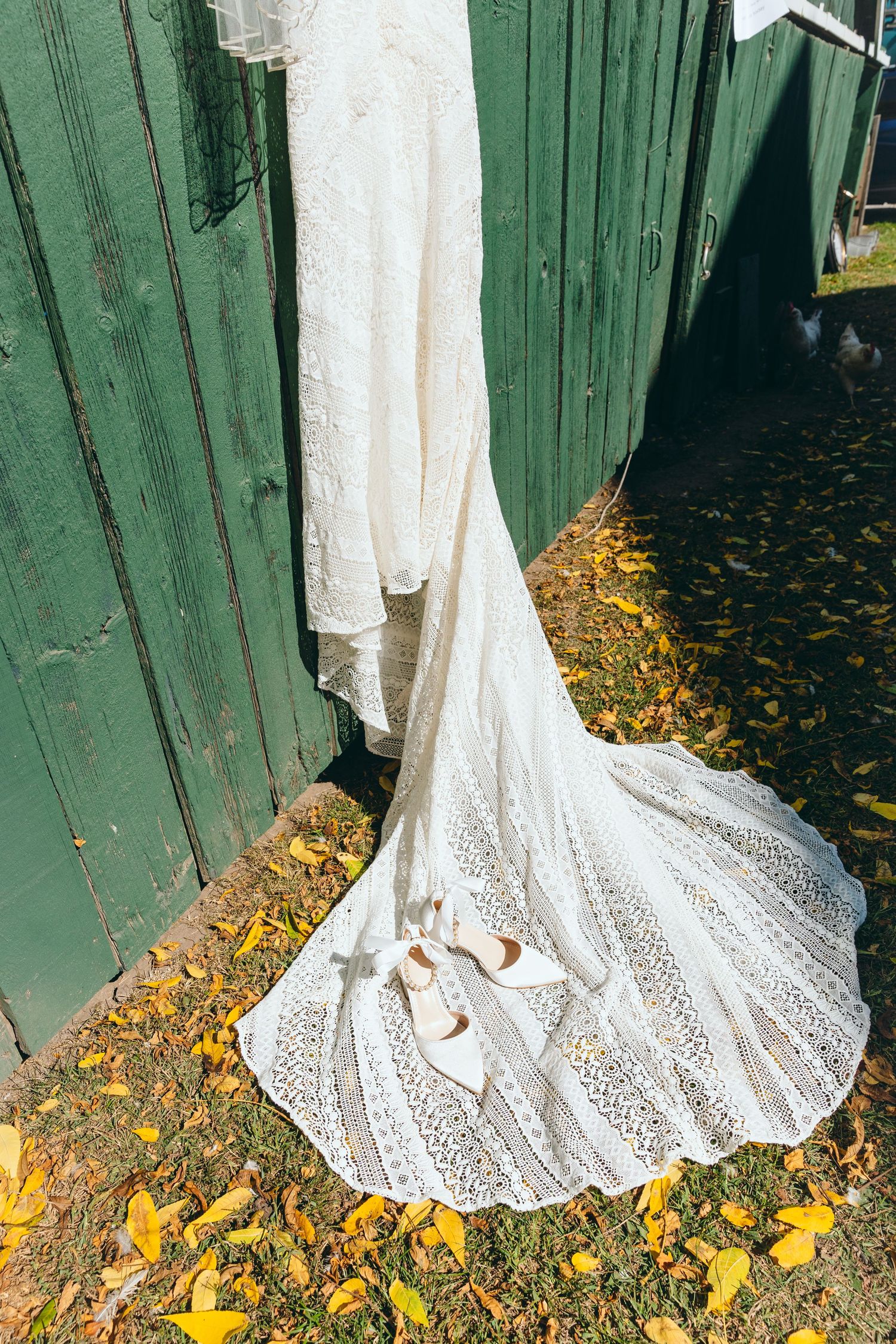 Detailed lace train of a white wedding dress spread over fallen autumn leaves.