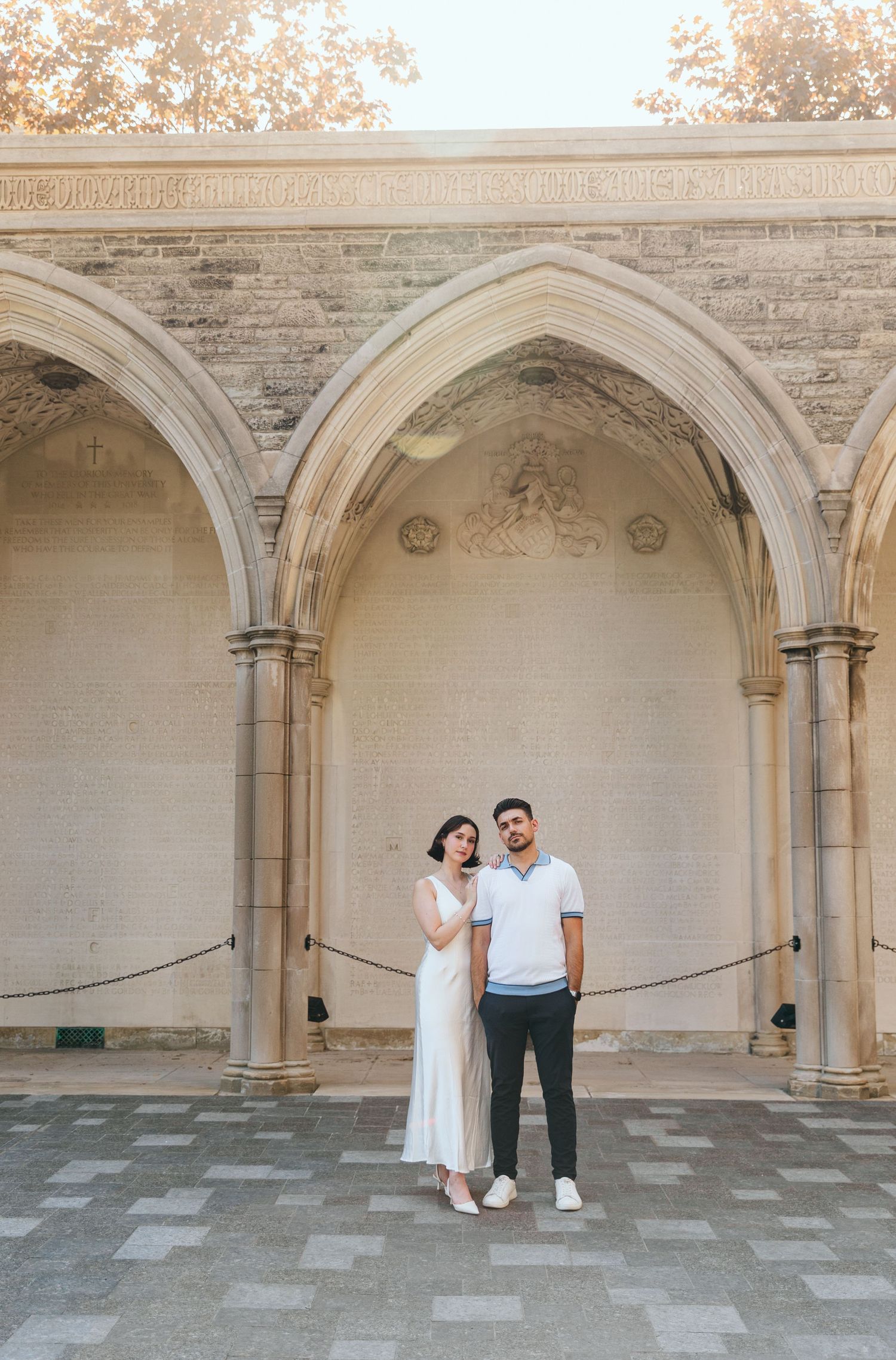 A couple poses together under a gothic stone archway in formal attire.