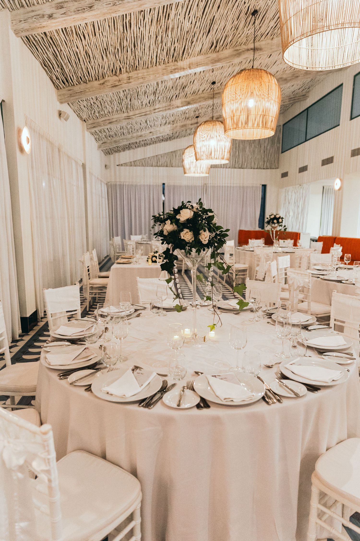 Elegant wedding reception setup with white linens and thatched roof decor.