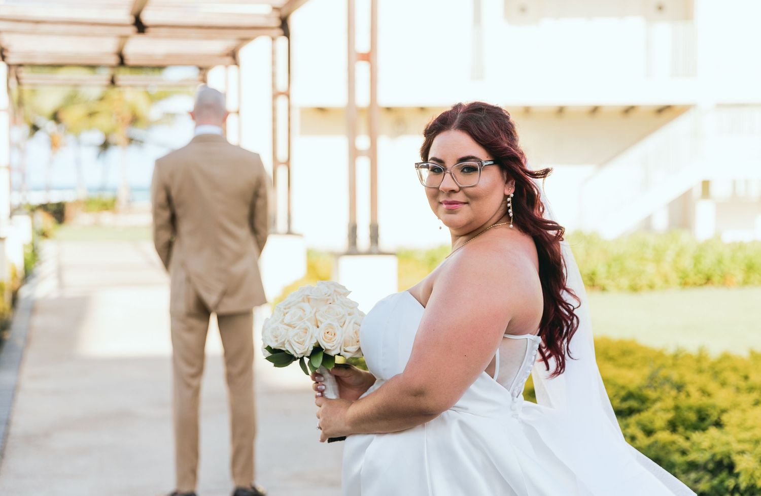 Wedding couple poses along a covered walkway with tropical landscaping.