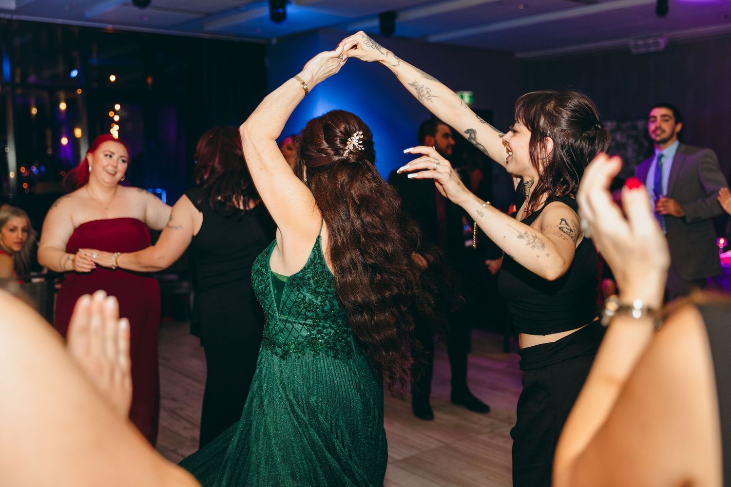 Wedding guests dancing under purple lighting at an evening reception celebration.
