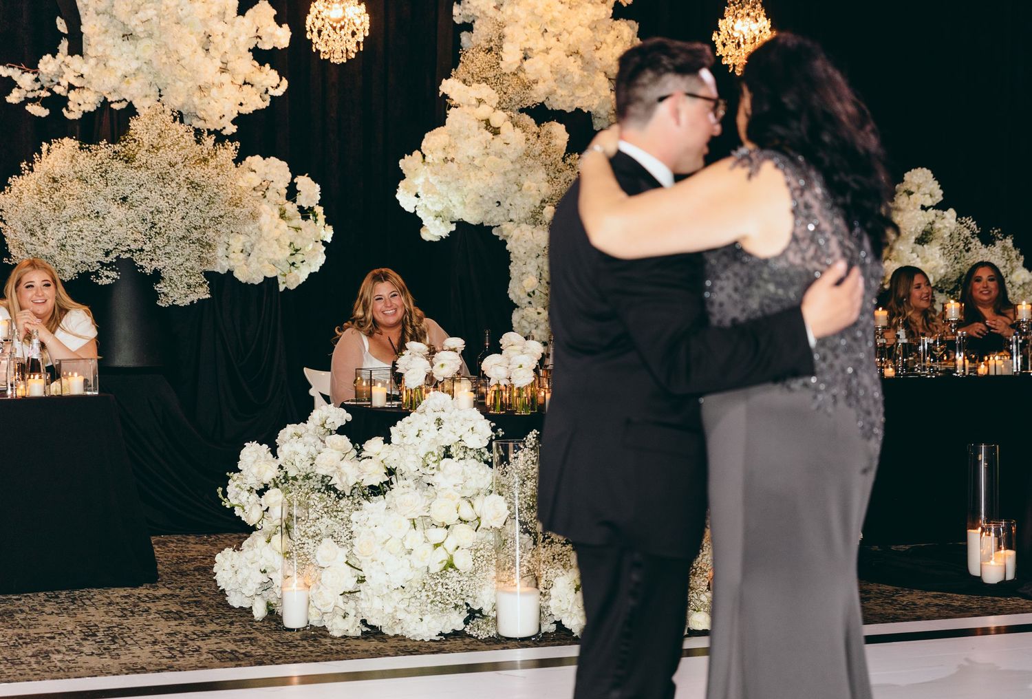 Couple dances in front of decorative white floral wall at wedding reception.