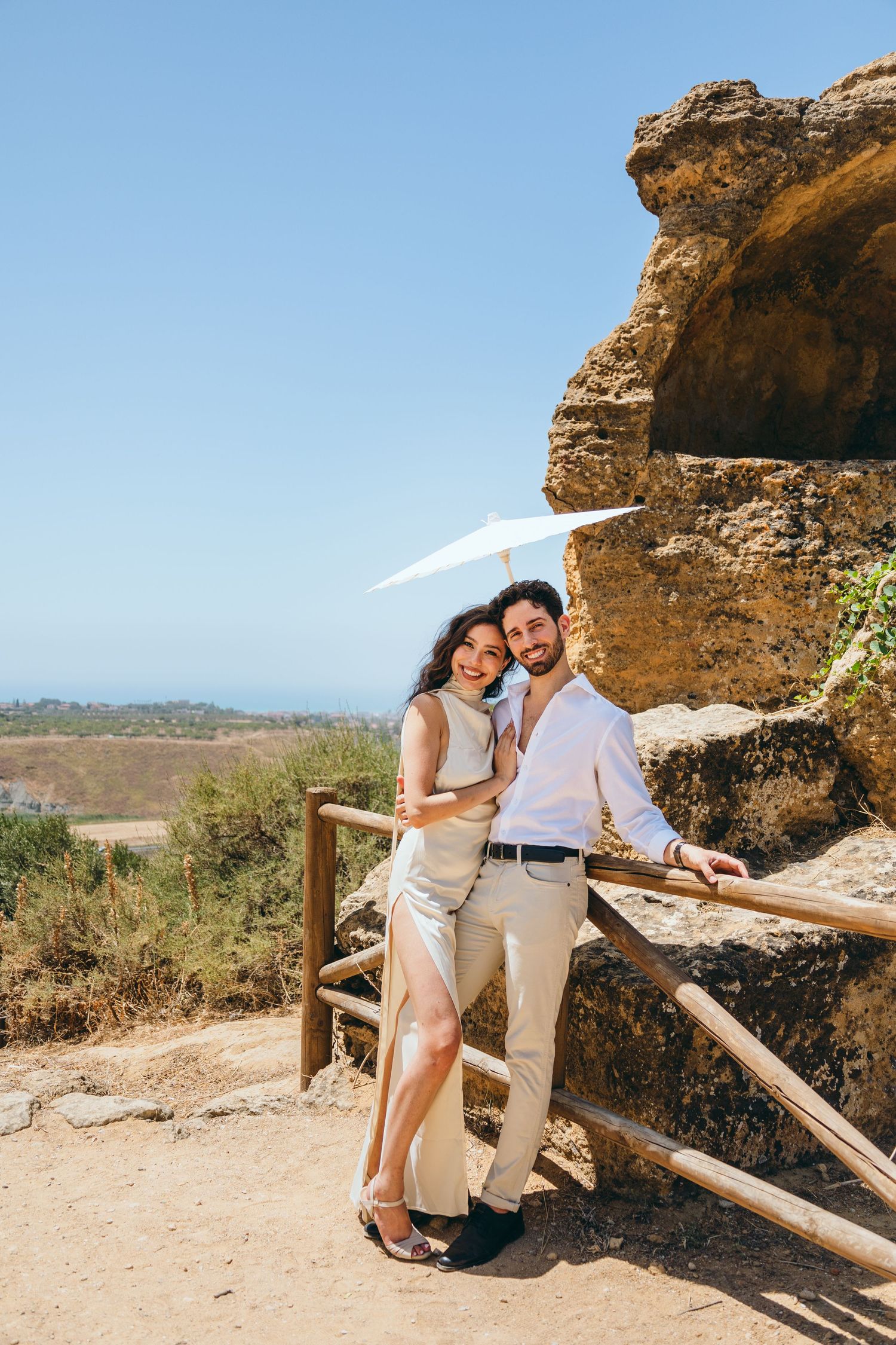 A couple shares intimate moments along a scenic overlook with rocky cliffs and wooden railings.