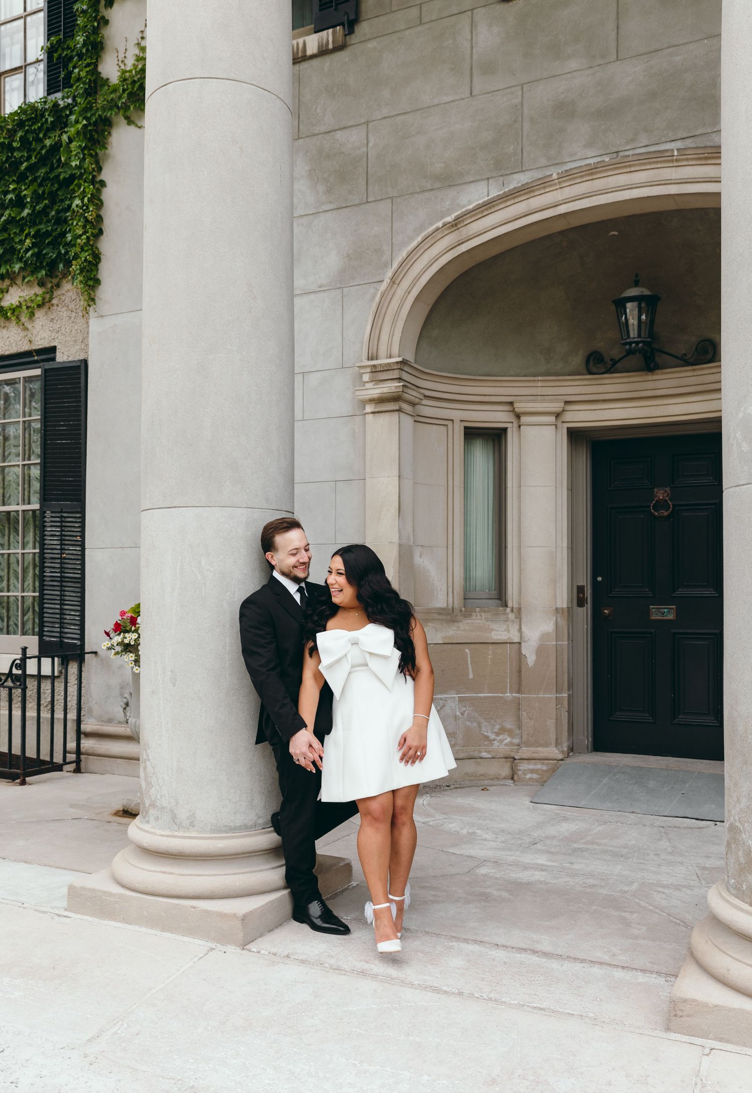 A couple poses together against a stone column entrance with ivy growing on the building.