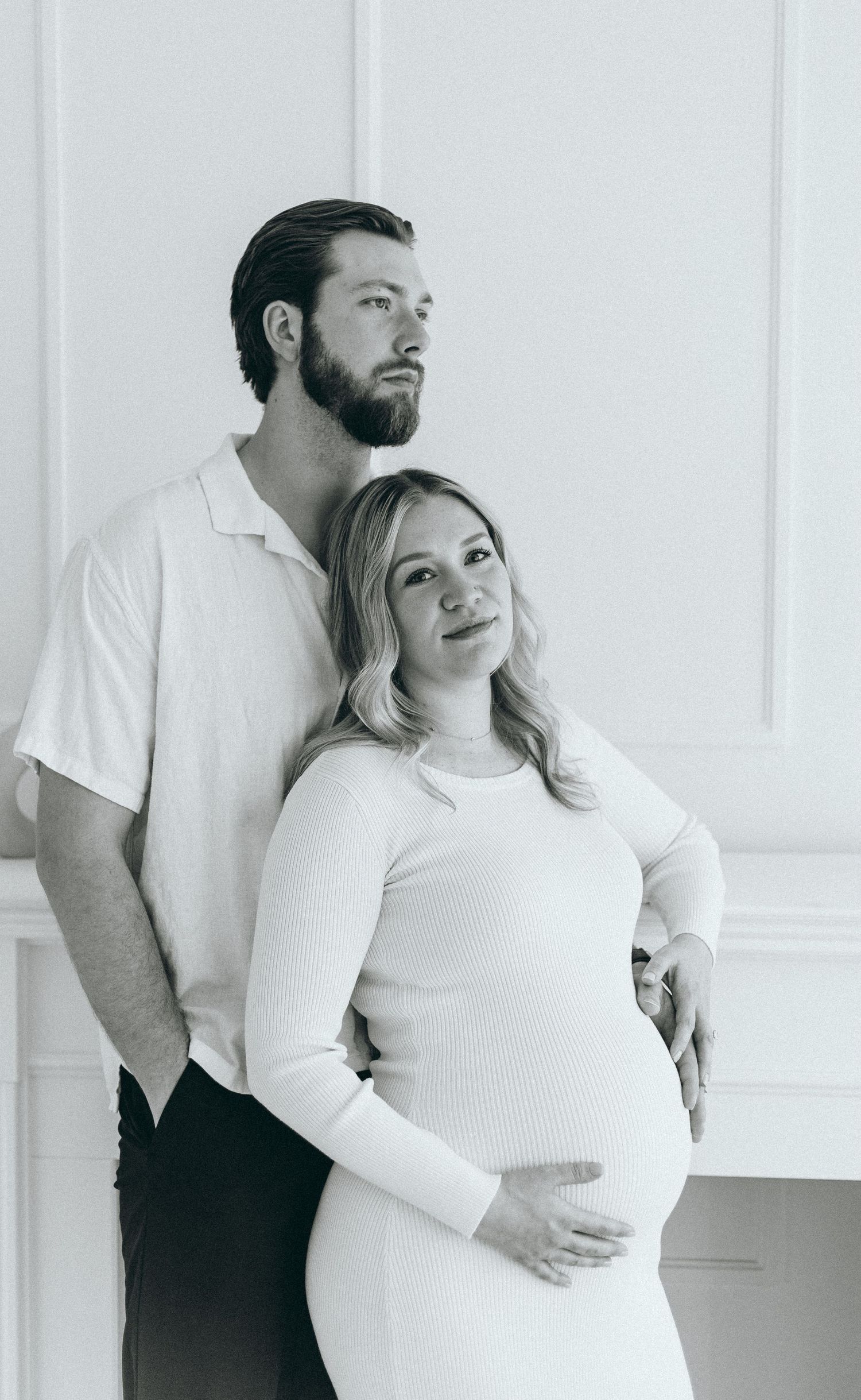 Minimalist maternity photos with couple in white against white wall.