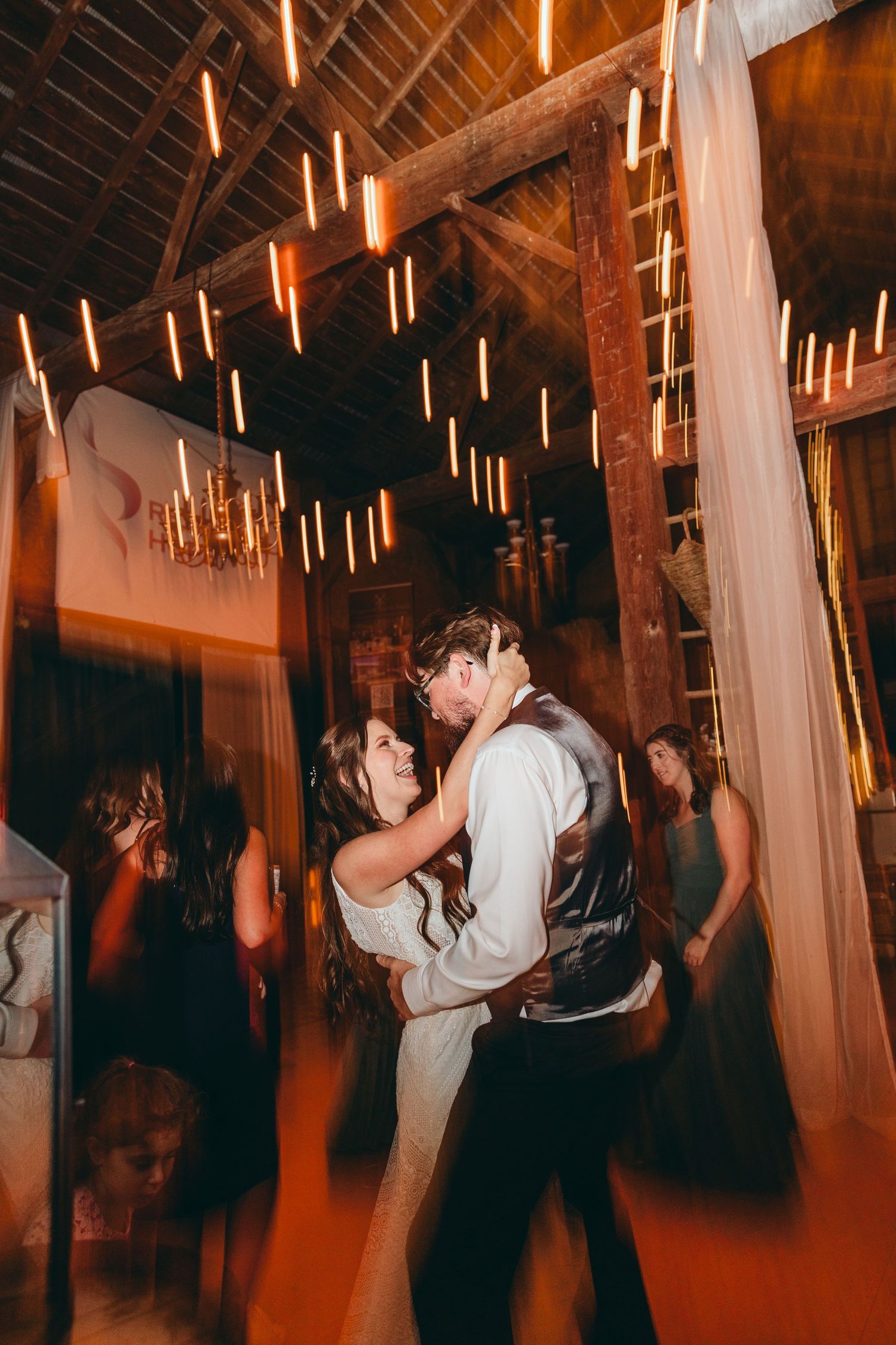 Wedding dance floor moments captured in a barn-style venue with hanging lights and white drapes.